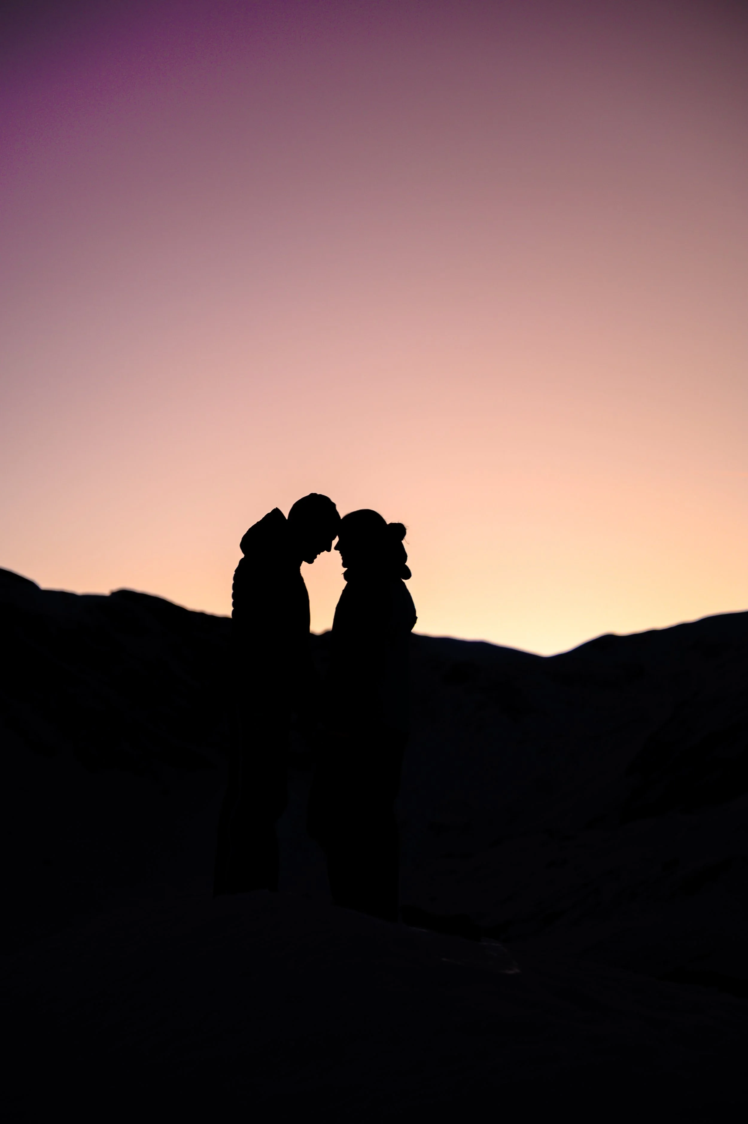 Silhouette eines Paares, das sich an einem Sonnenuntergang in einer bergigen Landschaft gegenübersteht.