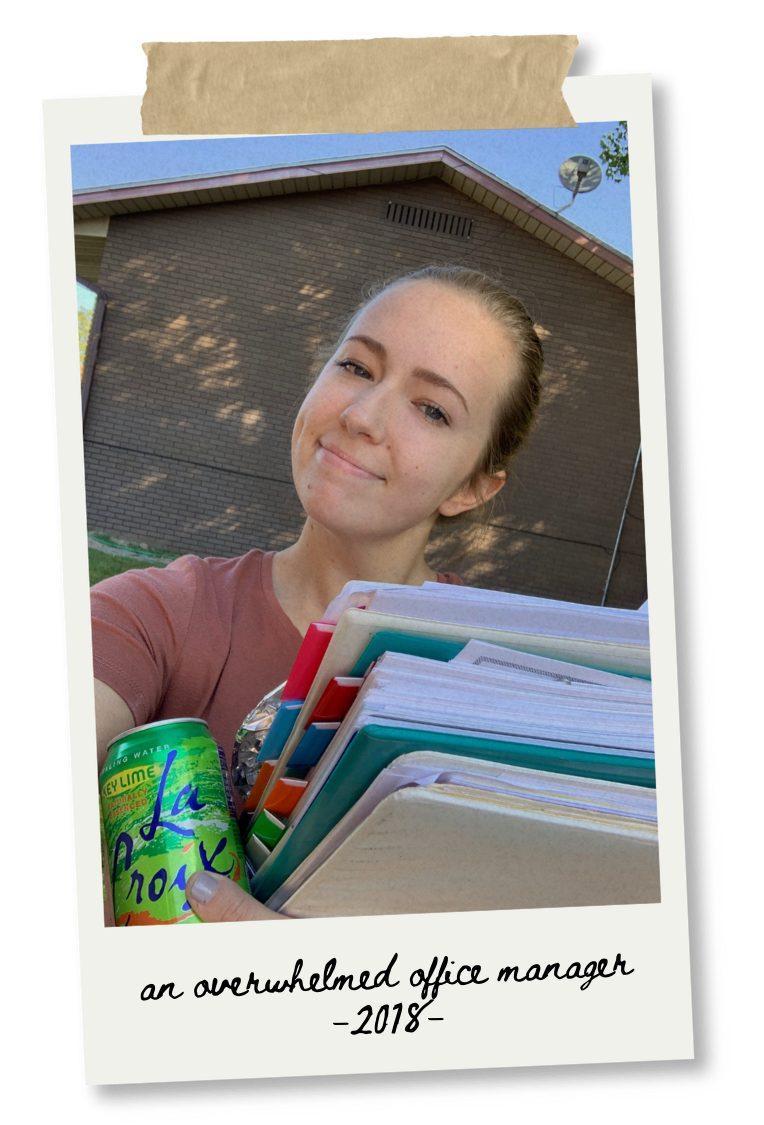 A young woman outside holding a large stack of files and a can of LaCroix sparkling water. She is smiling and standing in front of a brick building with a gabled roof. The photo has a handwritten caption that reads 'an overwhelmed office manager - 2018-'.