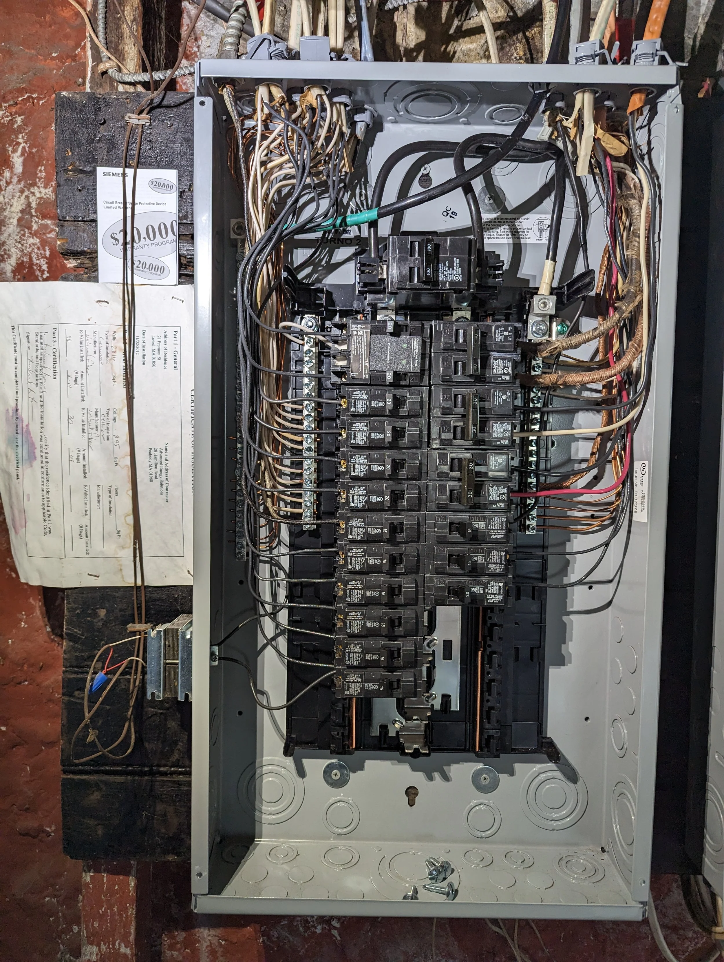 Open electrical breaker box with multiple circuit breakers, wires, and a grounding bar mounted inside a metal enclosure.