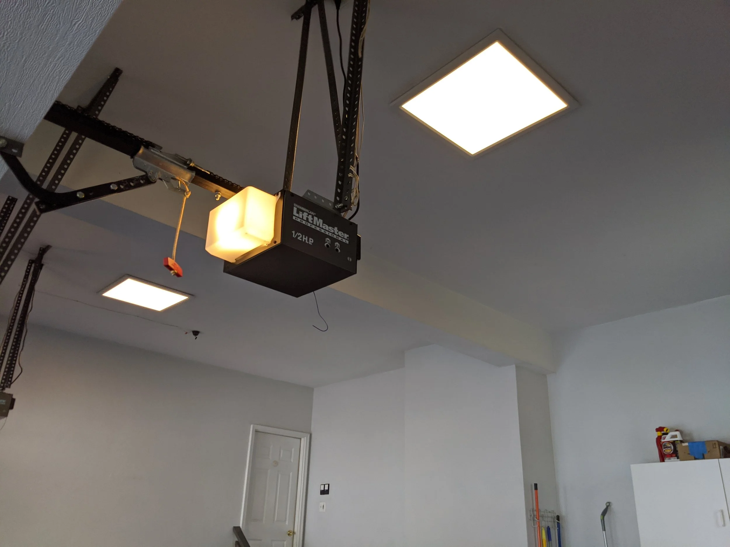 Garage with ceiling-mounted lift door opener, two ceiling lights, and cleaning supplies on a white cabinet.