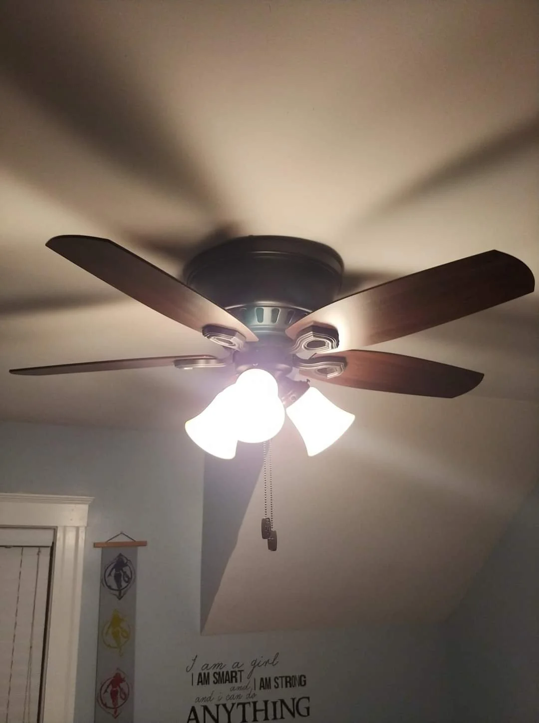 Ceiling fan with four wooden blades and four light fixtures hanging down, attached to a ceiling in a room.