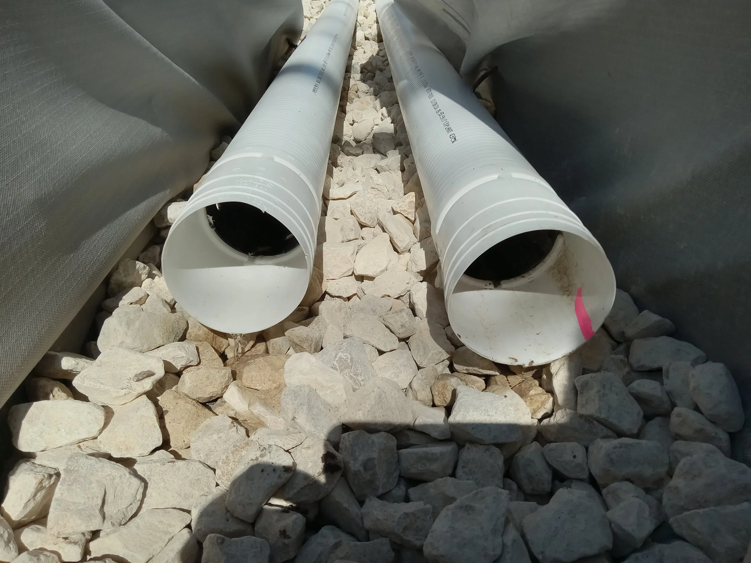 Two white PVC pipes lying on gravel between two pieces of black fabric or tarp.