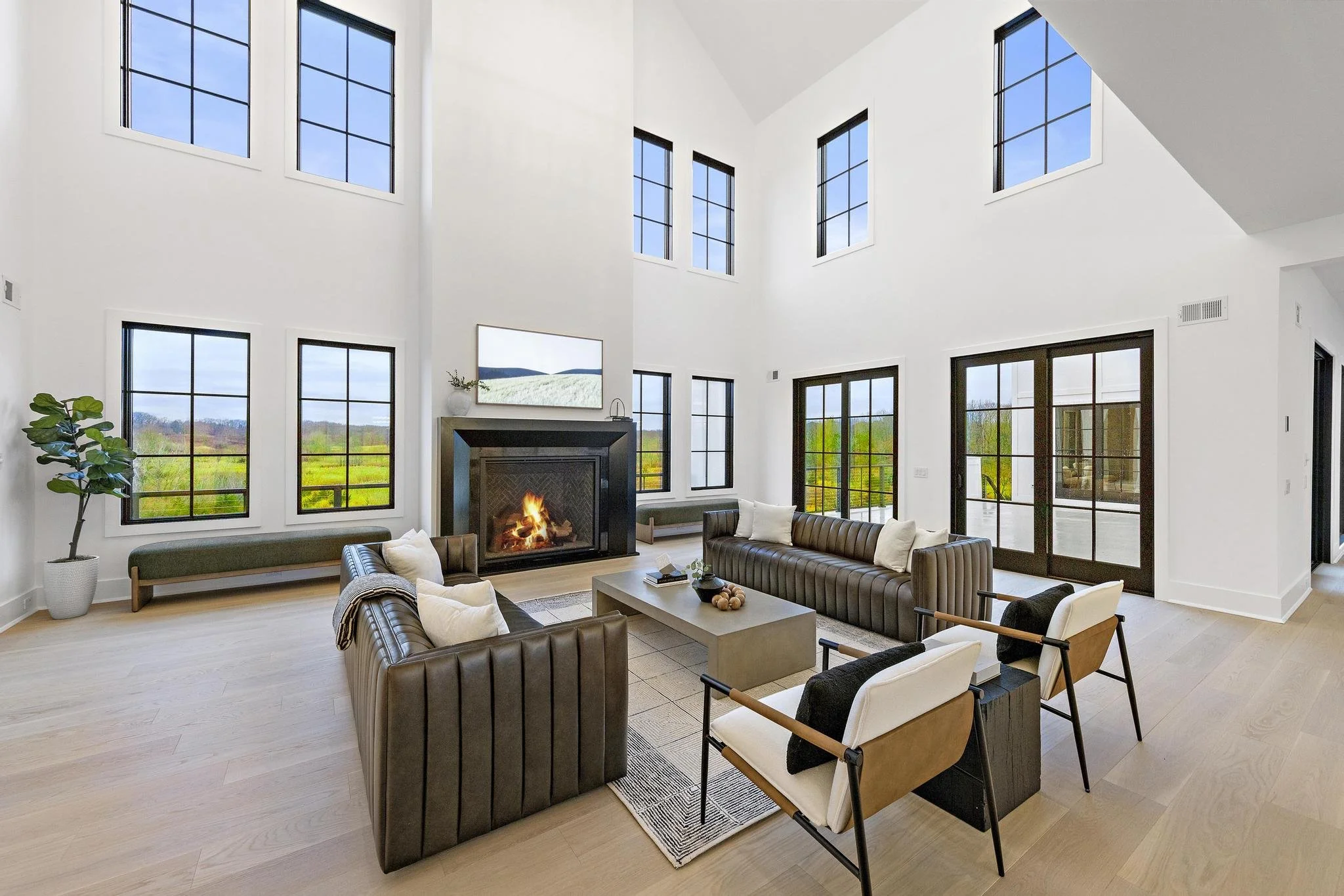 Spacious living room with high ceilings, large windows, a fireplace, modern furniture, and glass doors leading outside.