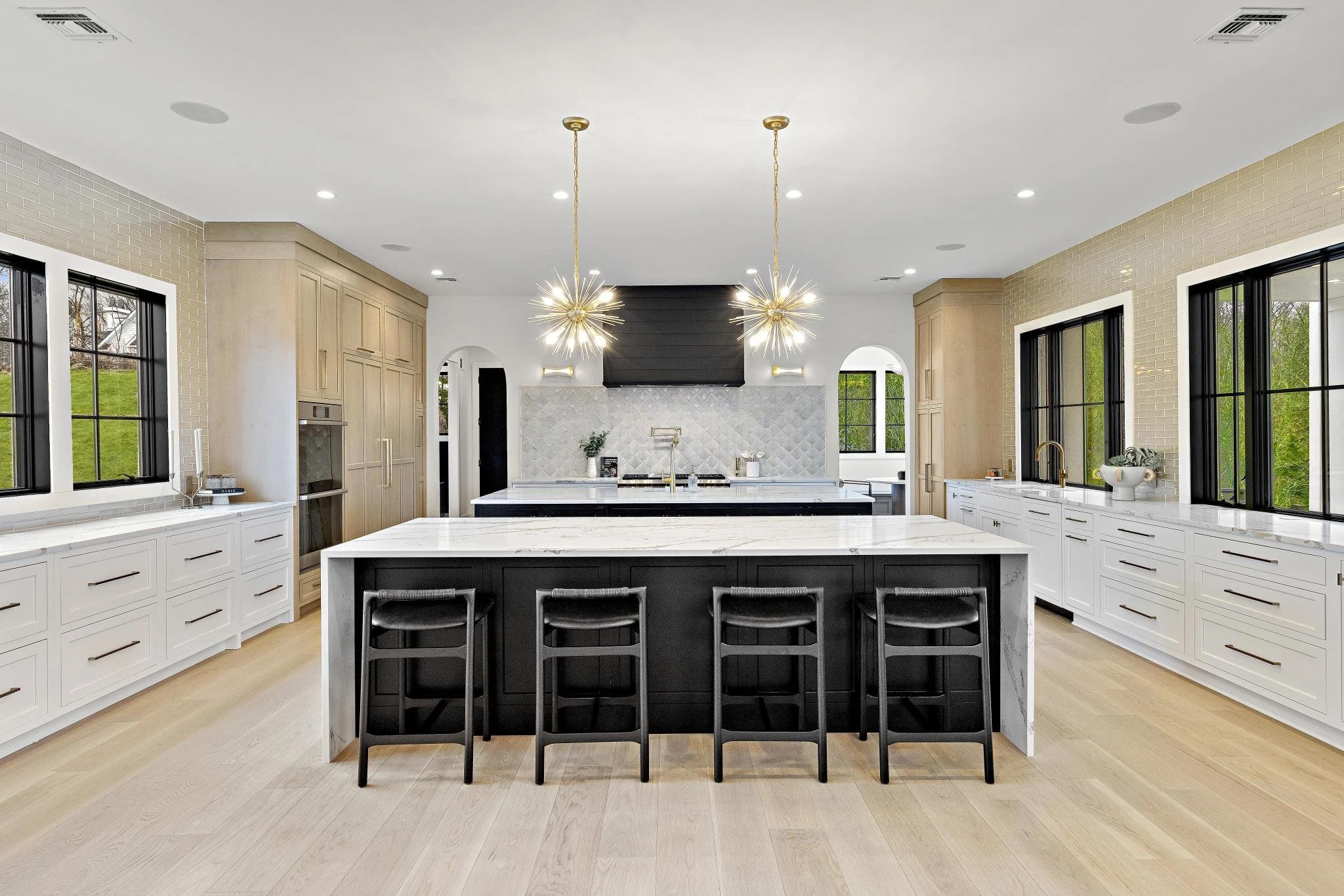 Modern kitchen with white and black cabinetry, a large island with a marble countertop, black stools, large windows, and pendant lights.