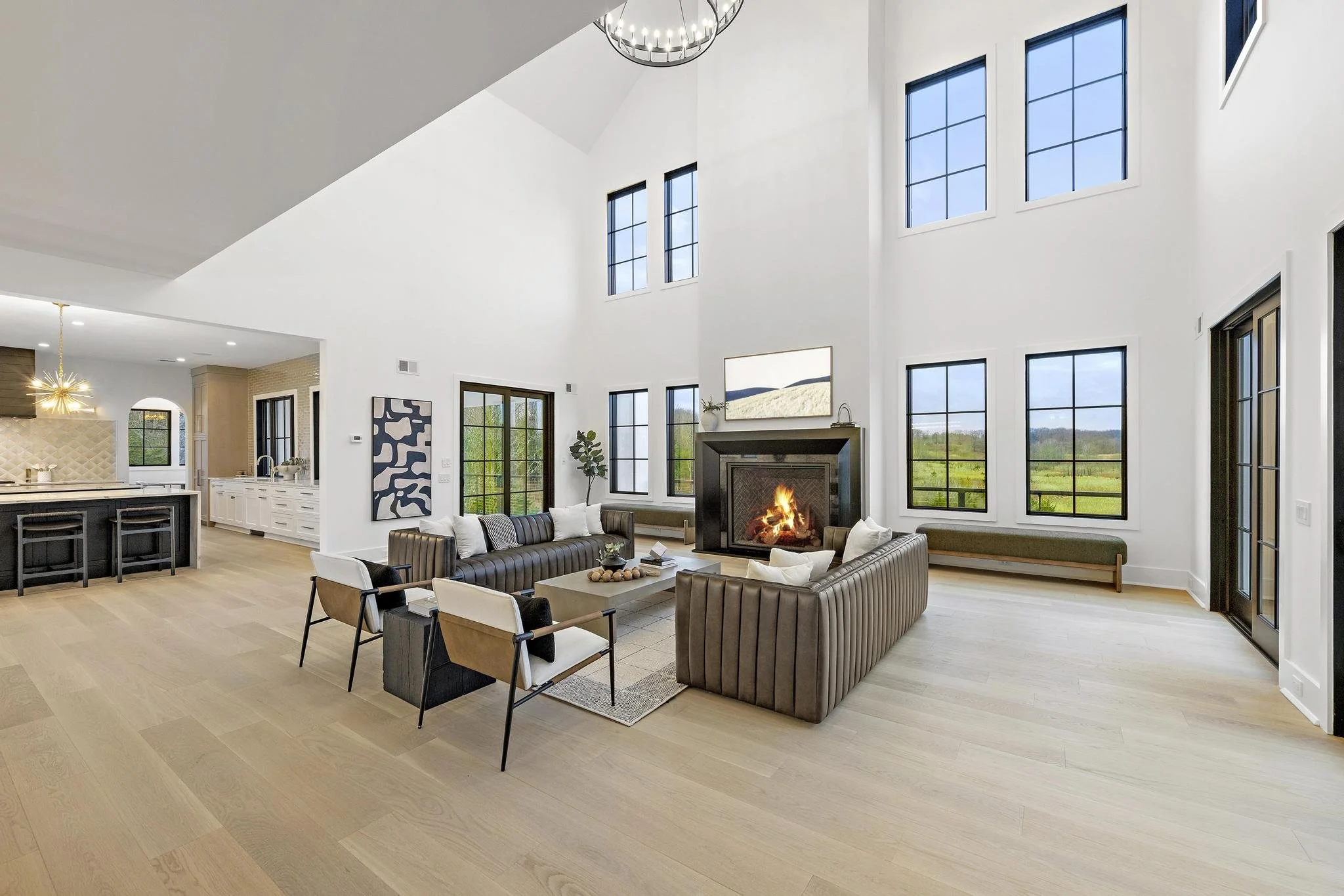Spacious, modern living room with high ceiling, large windows, a fireplace, and contemporary furniture.