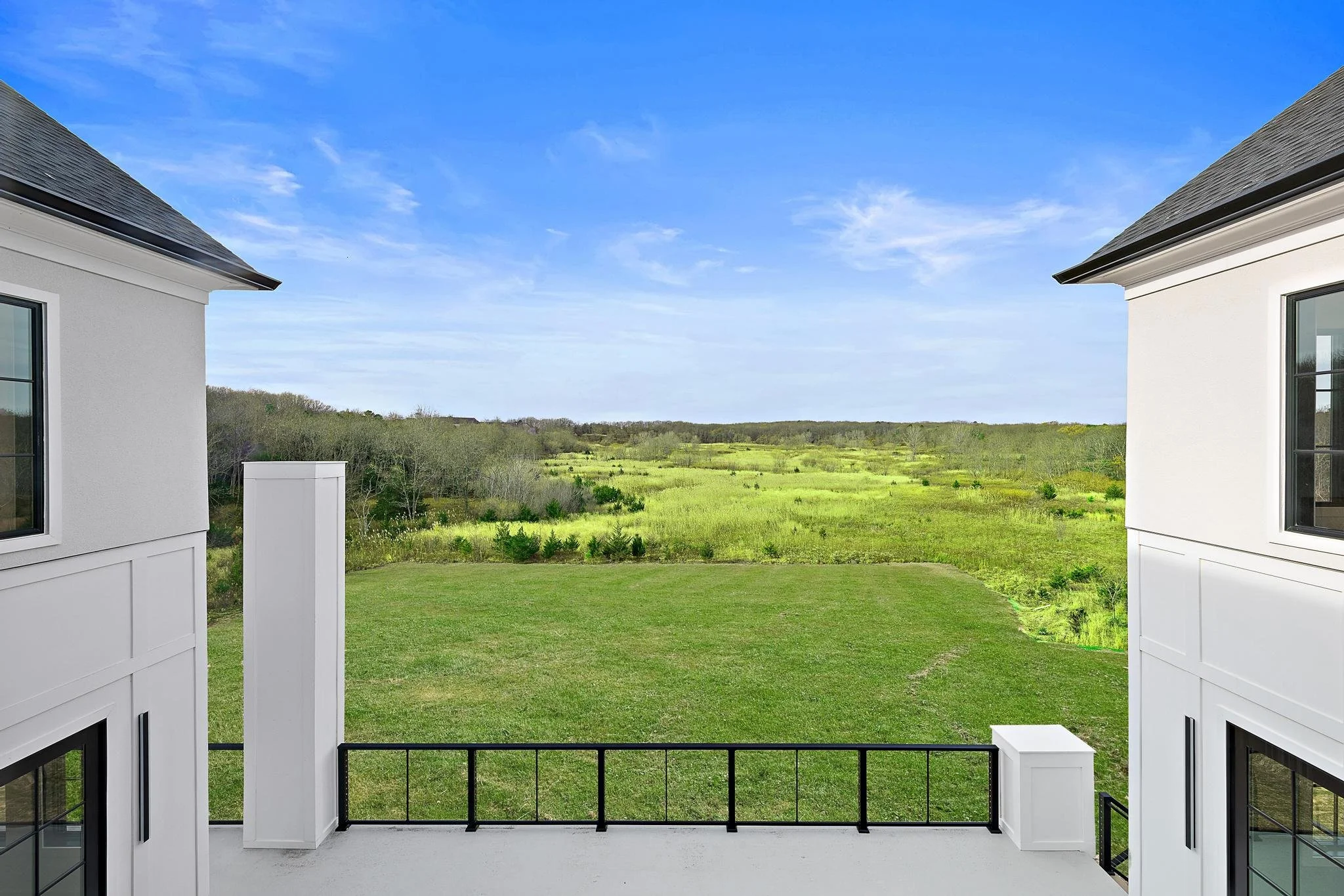 View from a balcony overlooking green fields and distant trees on a clear, sunny day.