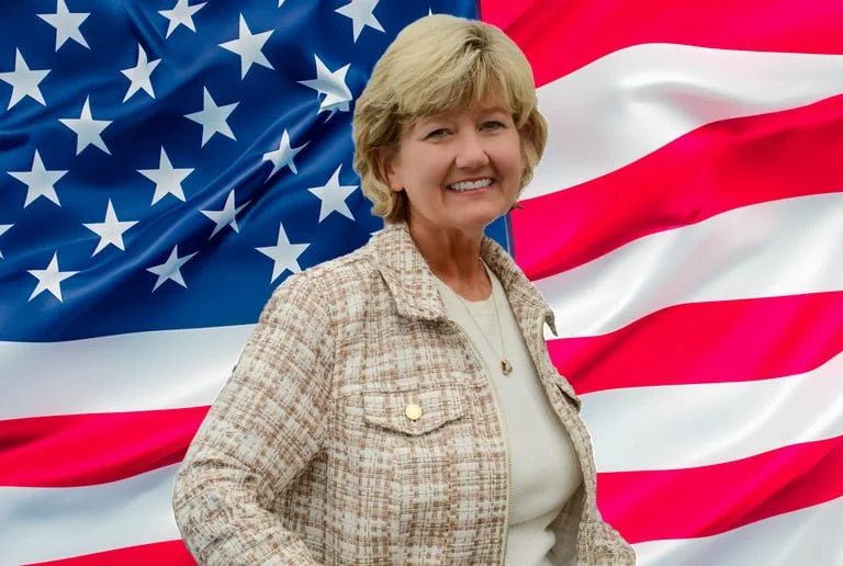 A smiling woman standing in front of an American flag backdrop.