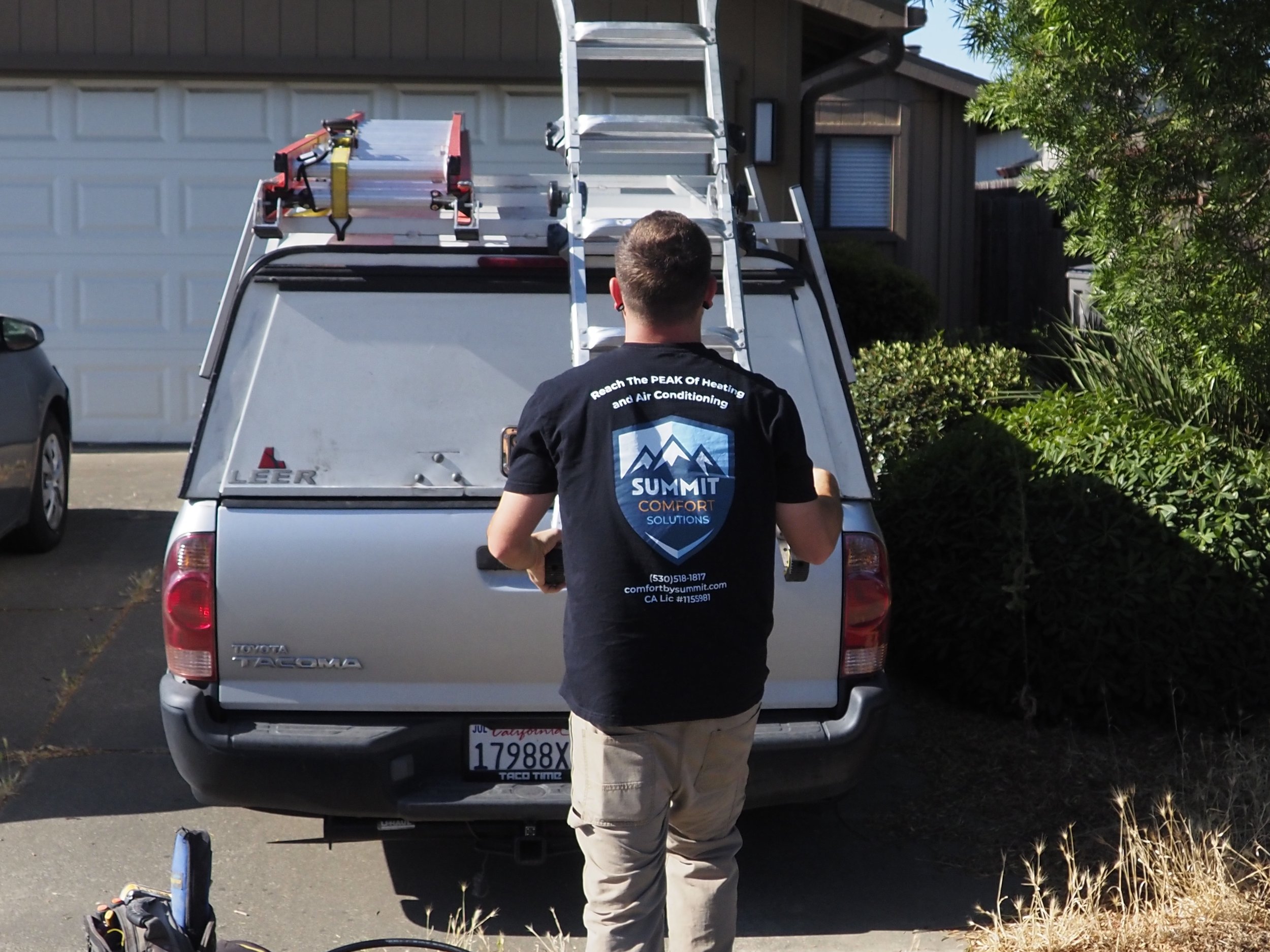 The image shows a technician taking a ladder off of a truck. The technician is wearing a shirt with the company logo on the back.