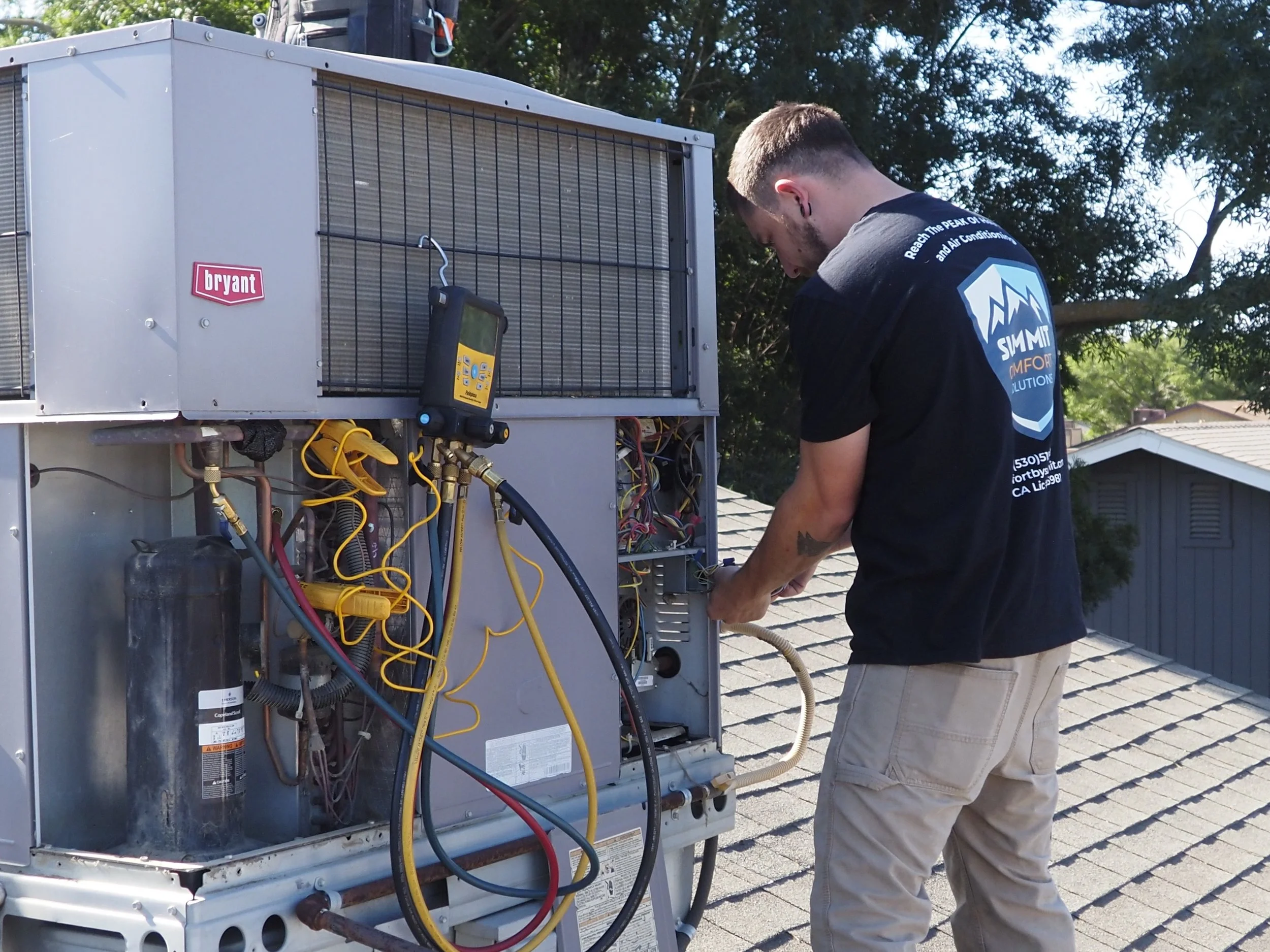 A technician inspecting and repairing an HVAC package unit installed on the roof of a house.