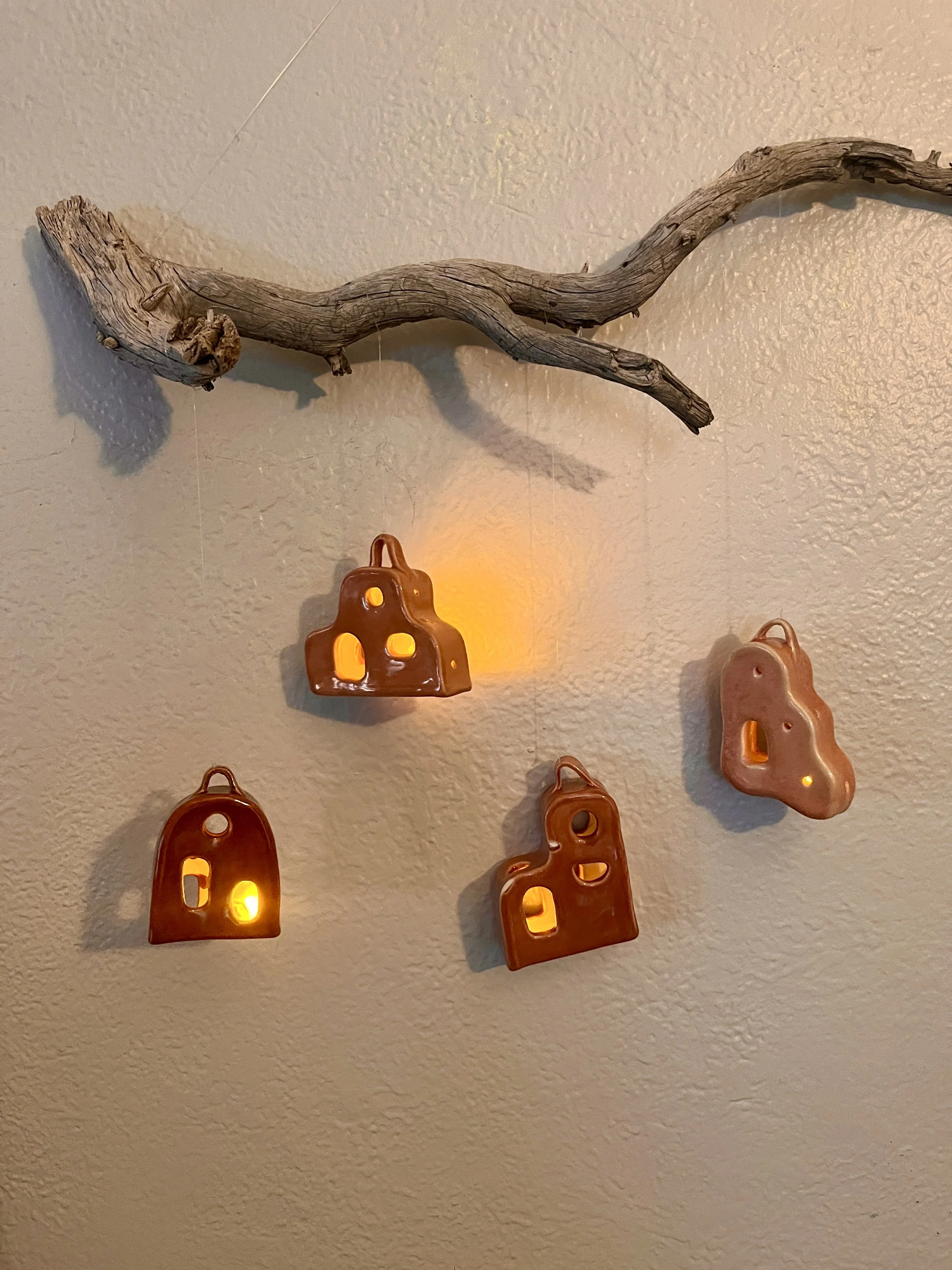 Decorative wall hanging with a piece of driftwood and five small lanterns shaped like gingerbread houses with warm yellow lights inside.