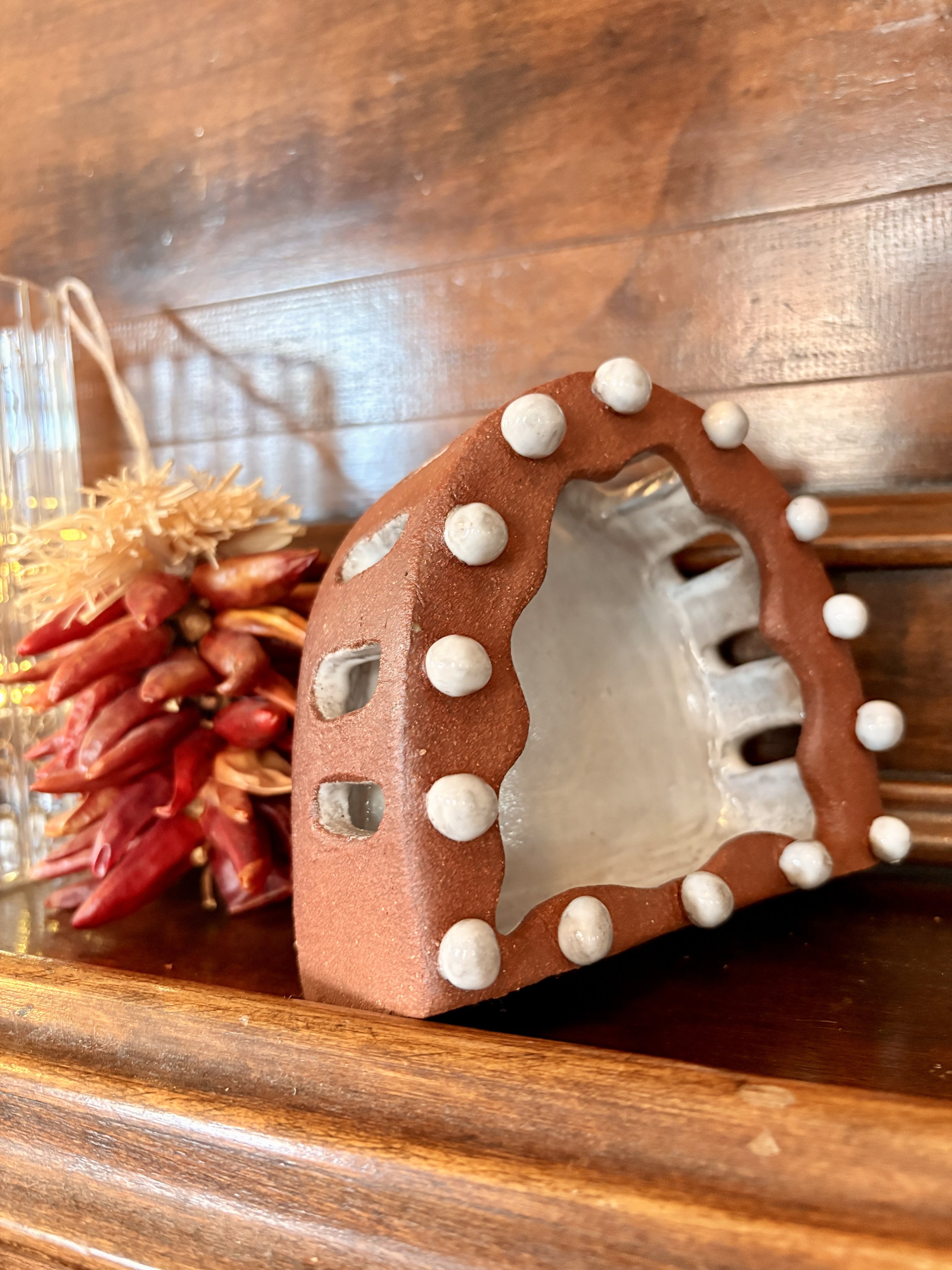 Decorative gingerbread house roof with white candy dots, placed on a wooden shelf beside a cluster of red and beige dried flowers.