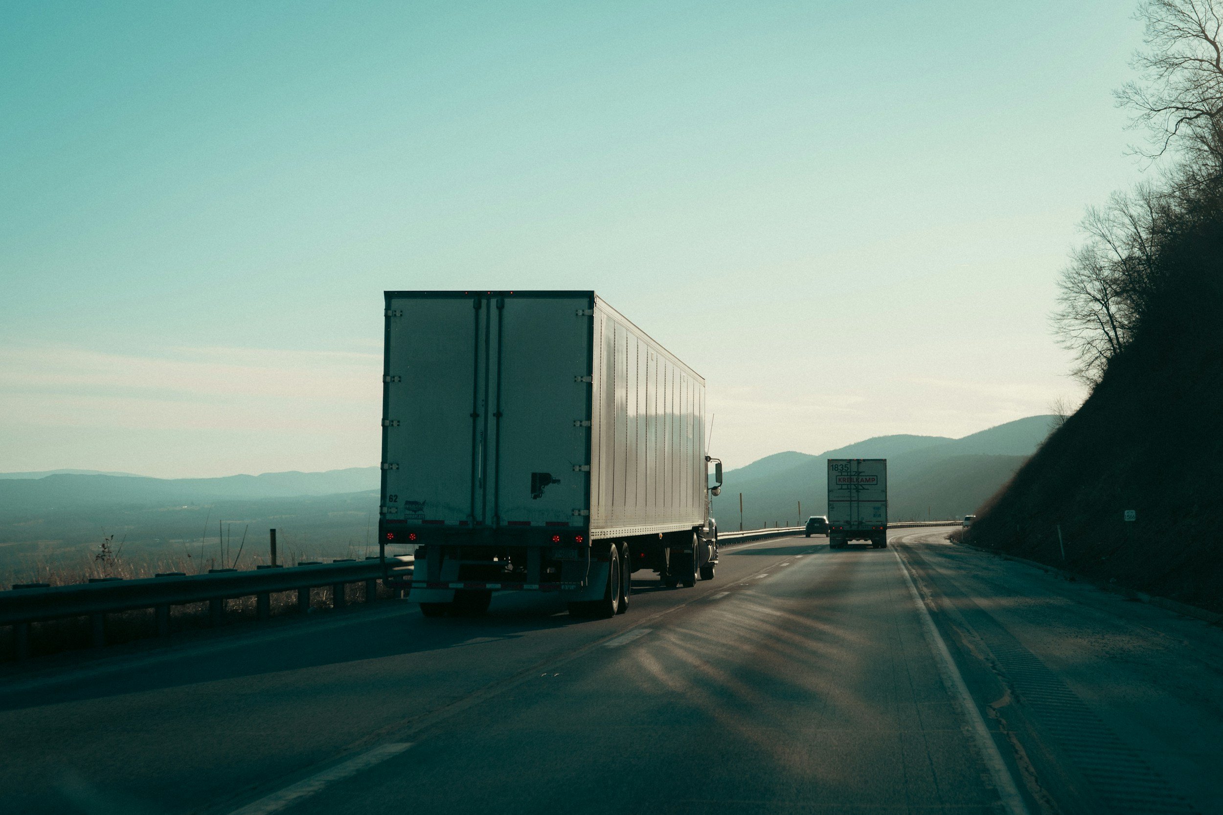 A highway with two trucks traveling on it, with a scenic view of mountains and a clear sky in the background.