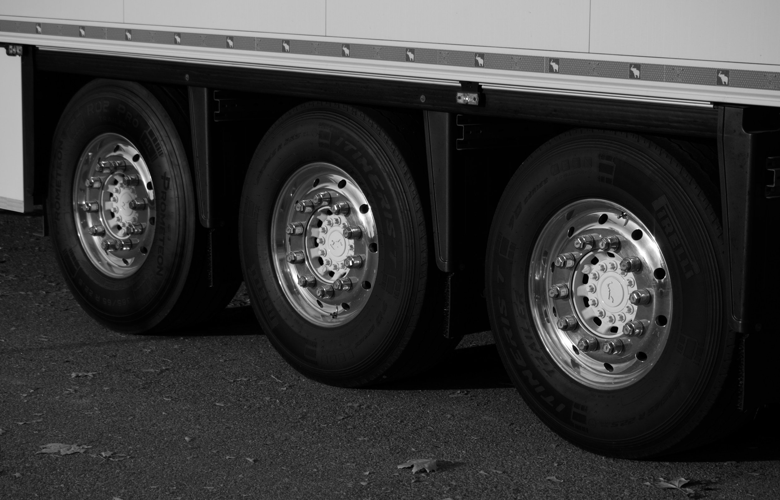 Close-up of three truck tires with shiny rims parked on a gravel surface.