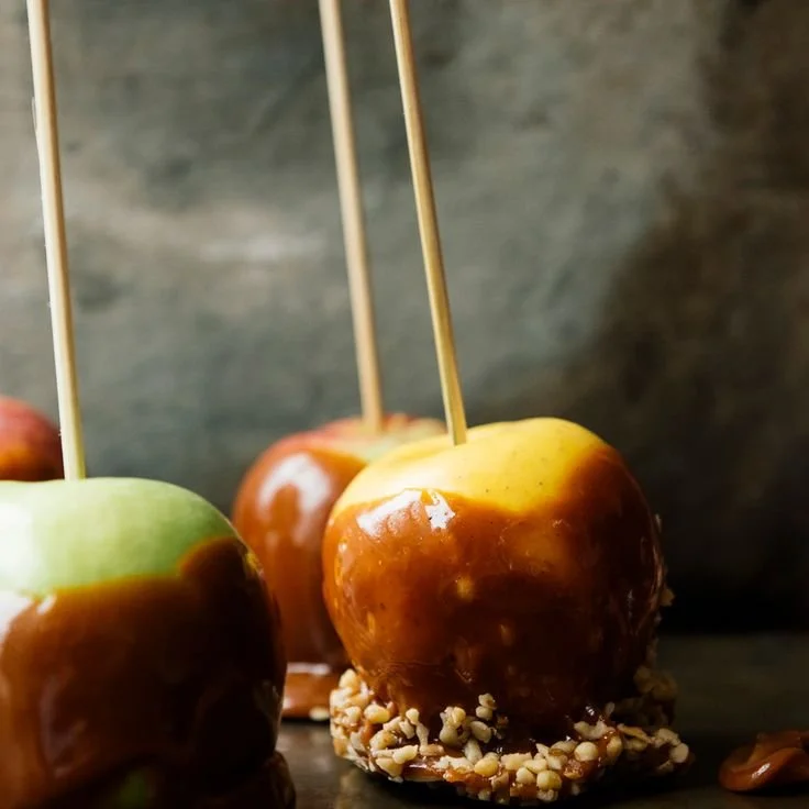 Caramel apples with chopped nuts on a dark surface with a blurred dark background.