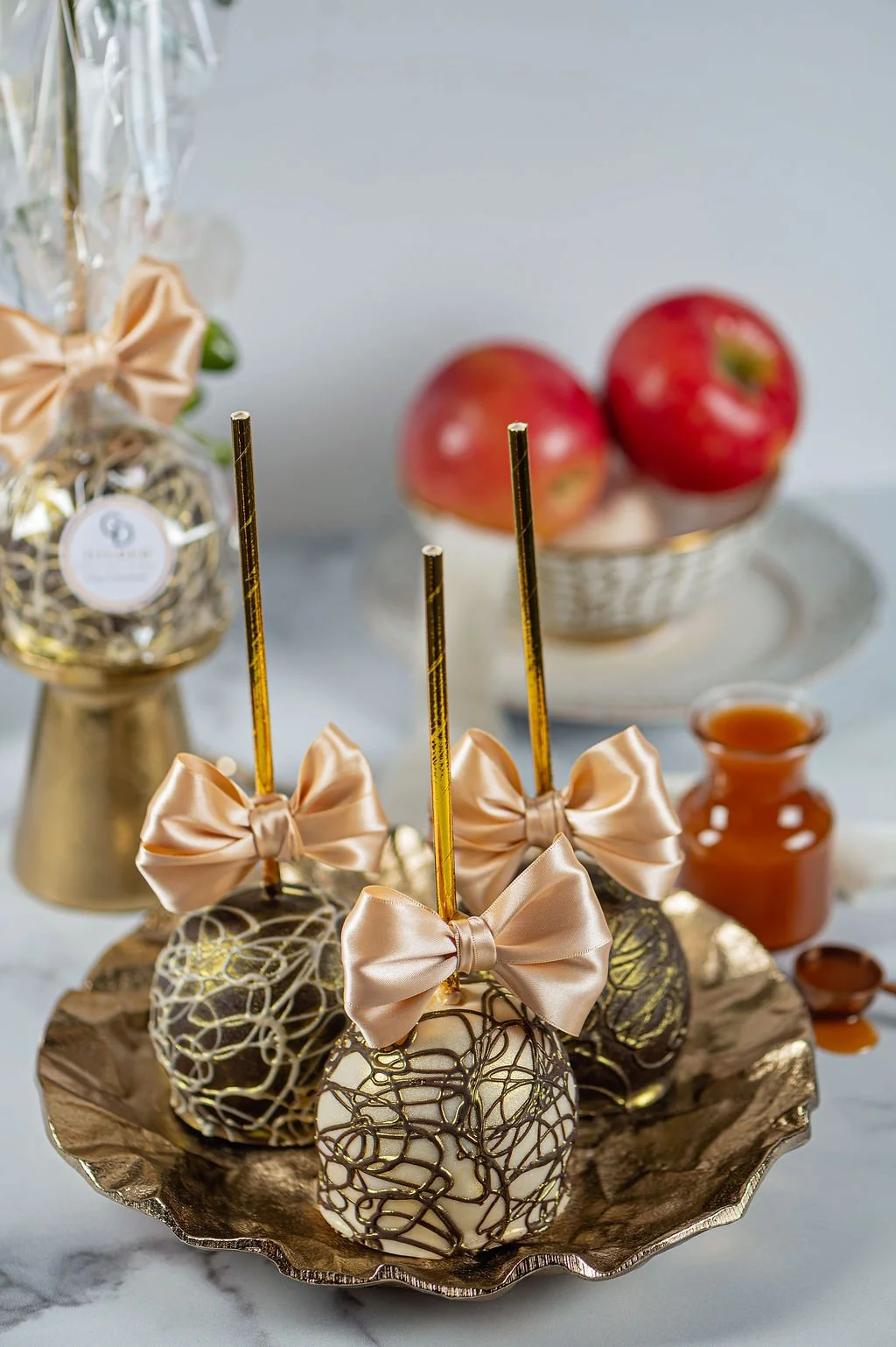 Elegant cake pops decorated with white and dark chocolate drizzle, each tied with a satin bow, on a metallic tray, with apples, honey jar, and festive decorations in the background.