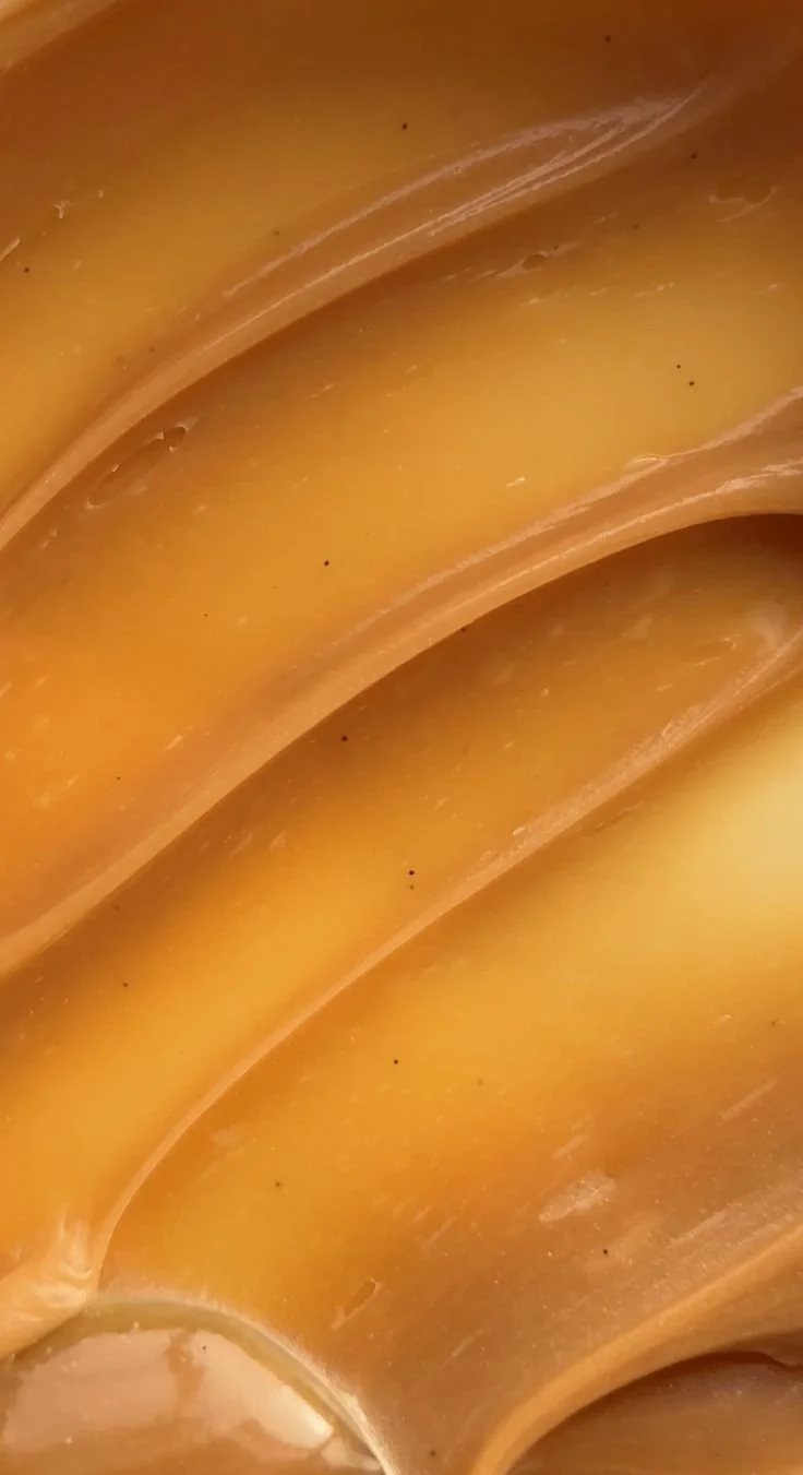 Close-up view of the surface of caramel candies showing their smooth, shiny texture and curves.