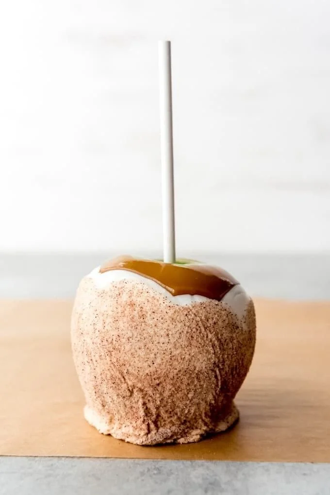 Caramel apple with a white coating and a white straw, placed on a wooden surface.