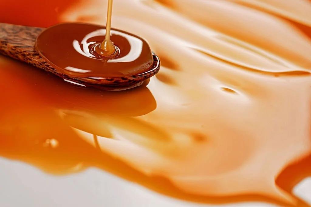 Close-up of caramel sauce being drizzled over a spoon, with caramel sauce spread on a surface.