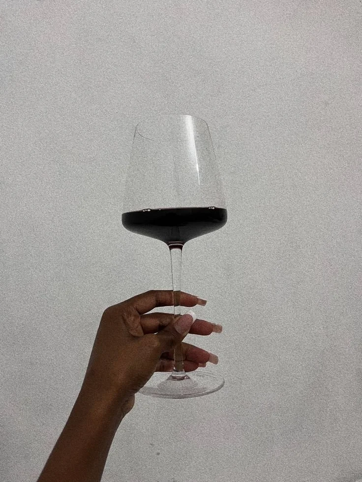 Hand holding a glass of red wine against a plain light-colored background.