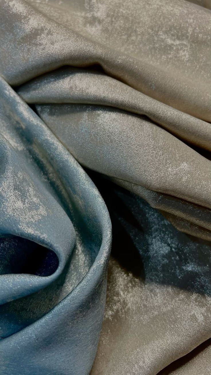 Close-up of light blue and silver satin fabric with a soft, shiny texture and some powdery dust on the surface.