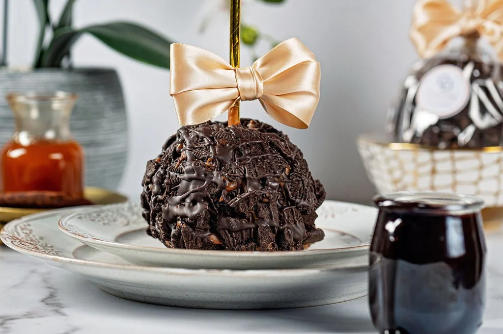 Chocolate cake ball decorated with a gold bow and drizzled with chocolate, placed on a decorative white plate.