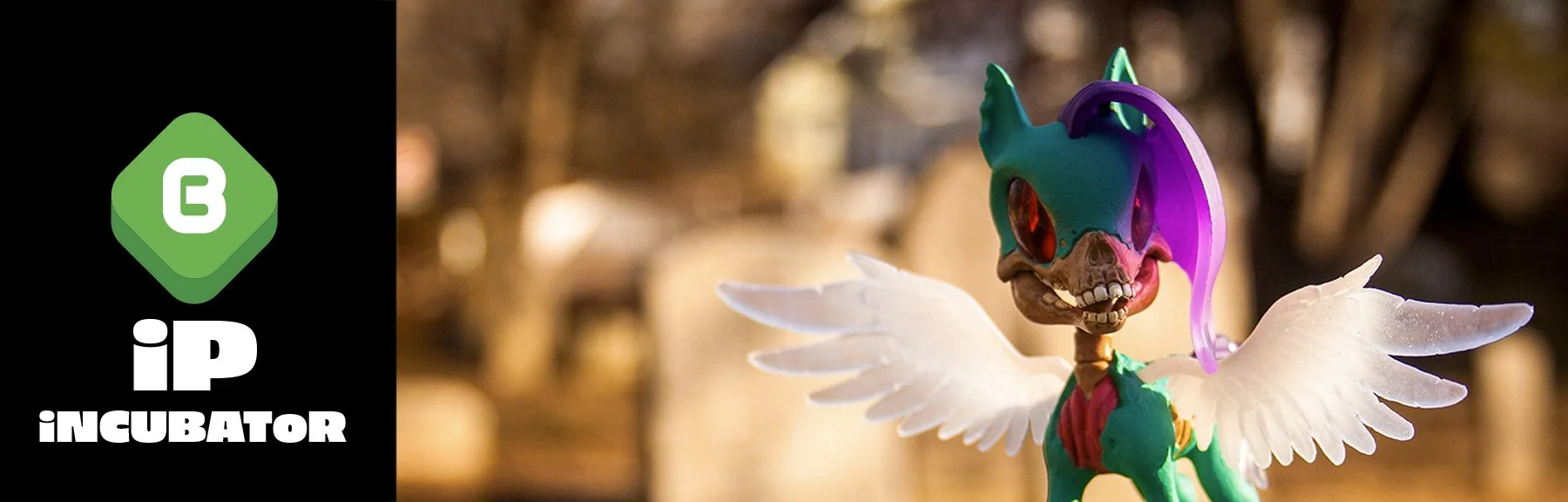 A fantasy creature with a skull head, wearing a colorful mask with pink, purple, and green, and white wings, standing outdoors with a blurred background.