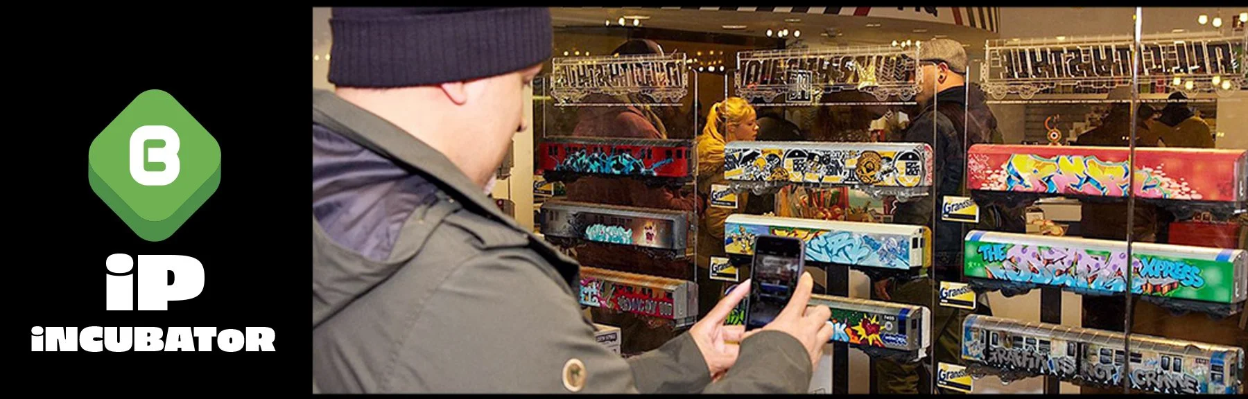 A man in a gray jacket and beanie takes a photo of a display of colorful electronic game boards inside a store, with other shoppers visible through the glass window.