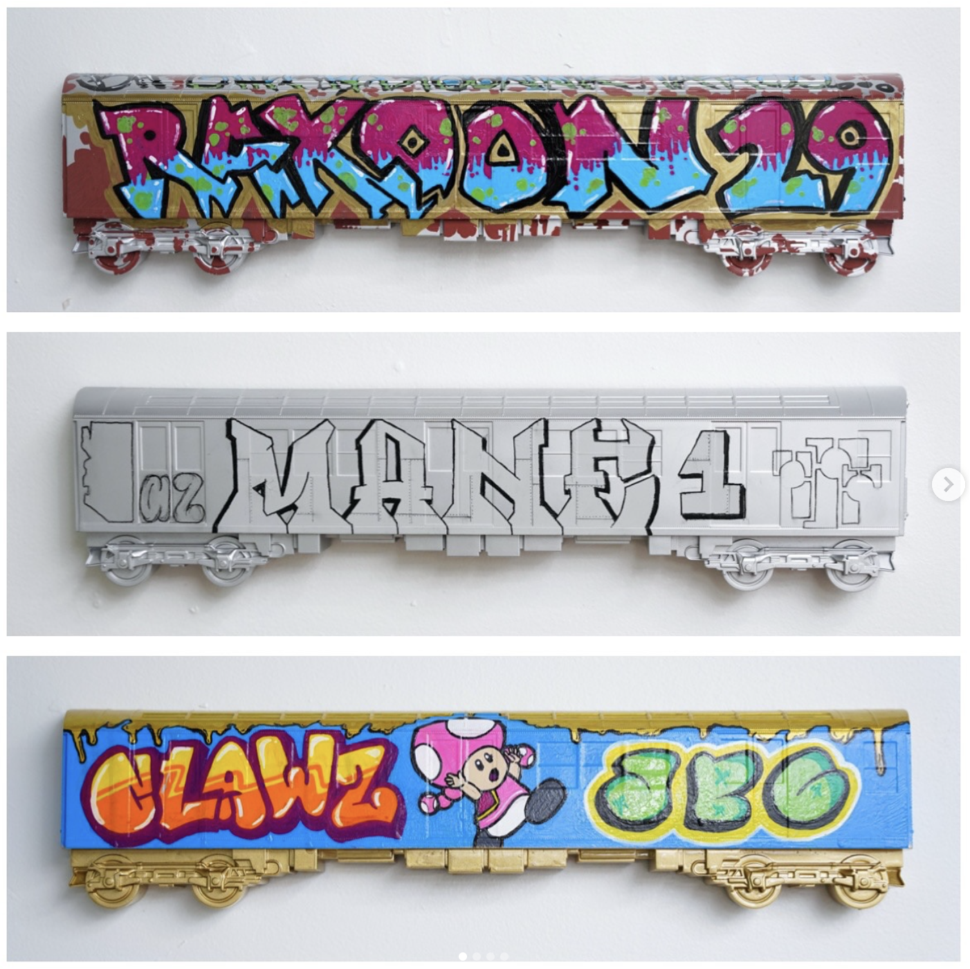 Three toy train cars with graffiti art painted on them. The top train car has colorful graffiti lettering on a red background, the middle car is unpainted with outline graffiti, and the bottom car features graffiti spelling 'CLAWR' in red and yellow 