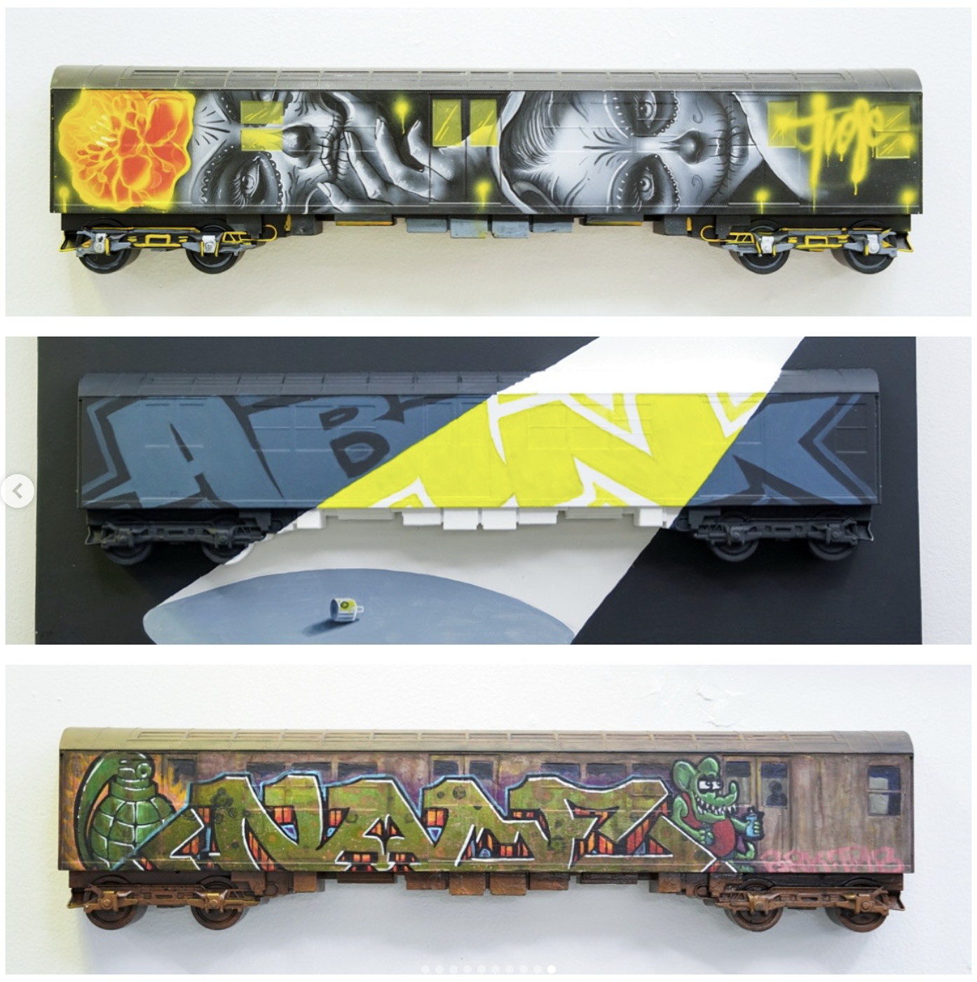 Three model train cars decorated with graffiti-style street art, each with distinct designs and colors.