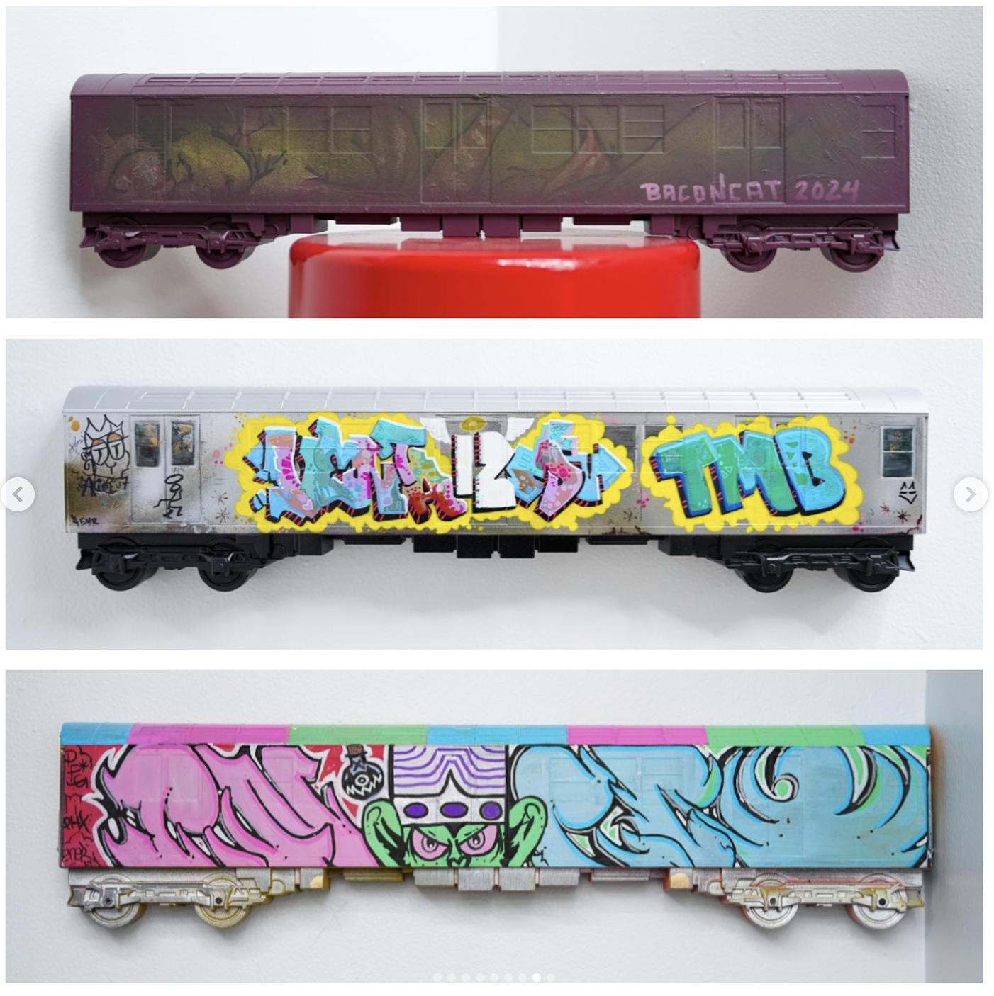 Three model train cars decorated with graffiti art mounted on the wall.