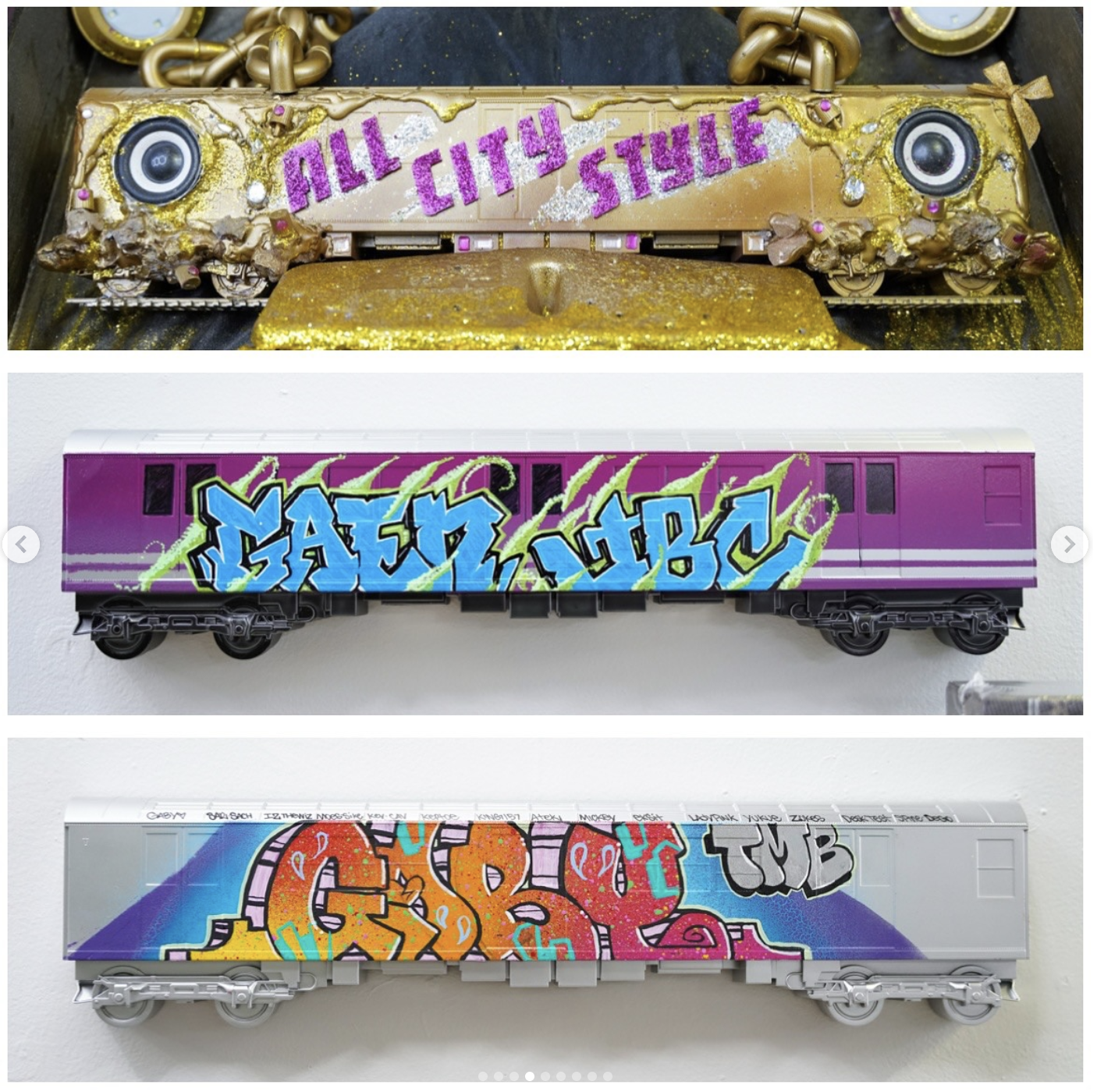 Three model train cars with graffiti art on them. The top train car is gold with purple glitter letters spelling 'ALL CITY STYLE.' The middle train car is purple with blue and green graffiti reading 'GASM CLUB.' The bottom train car is silver with co