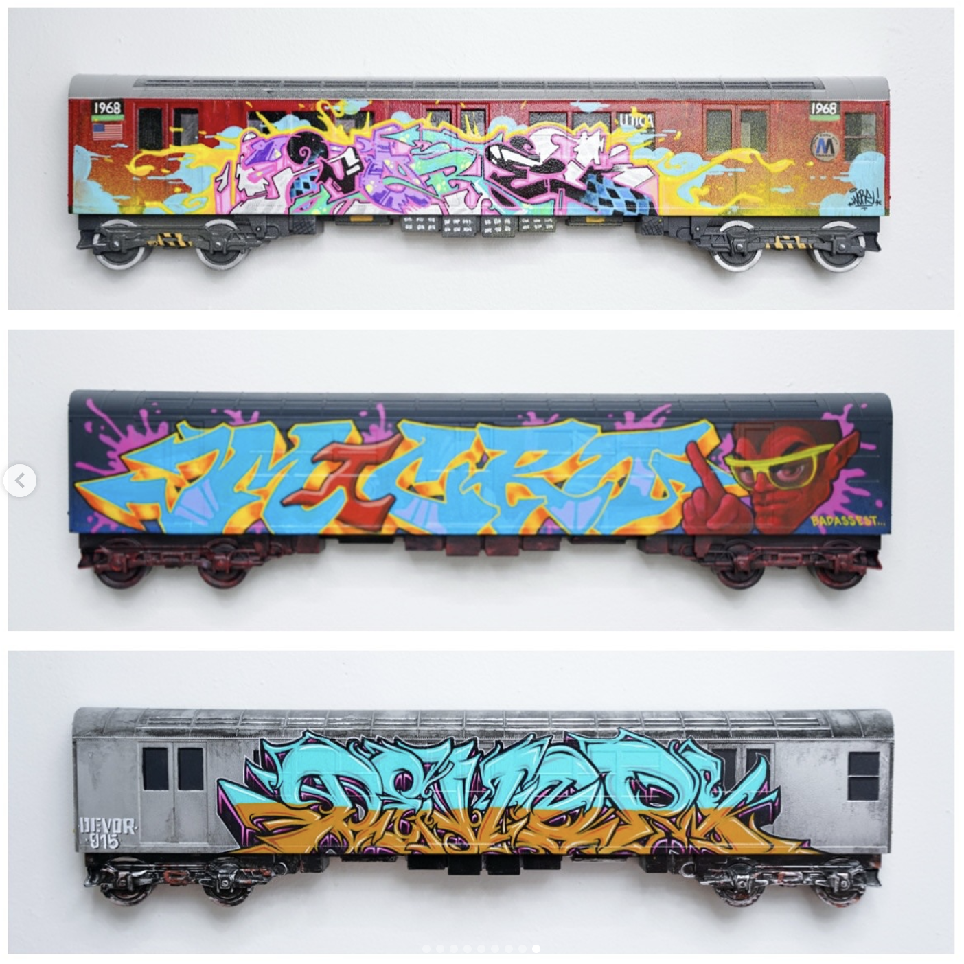 Three model train cars with graffiti art on them. The first train car has a colorful graffiti piece on a red background. The second train car features a graffiti piece with a cartoonish character wearing glasses on a black background. The third train