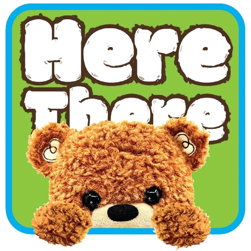 A Tickle Me Elmo toy with a teddy bear face and a green background that says "Here Tickle" in large white letters with black outlines, enclosed in a blue border.