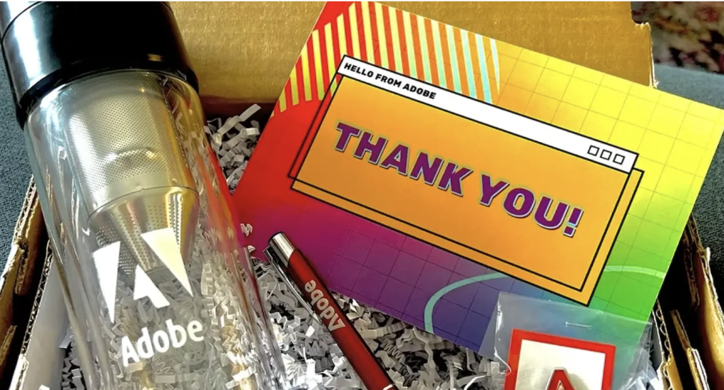 A thank you card, an Adobe Spire water bottle, a red Sharpie marker, and a small packet with a paper clip, all in a cardboard gift box.
