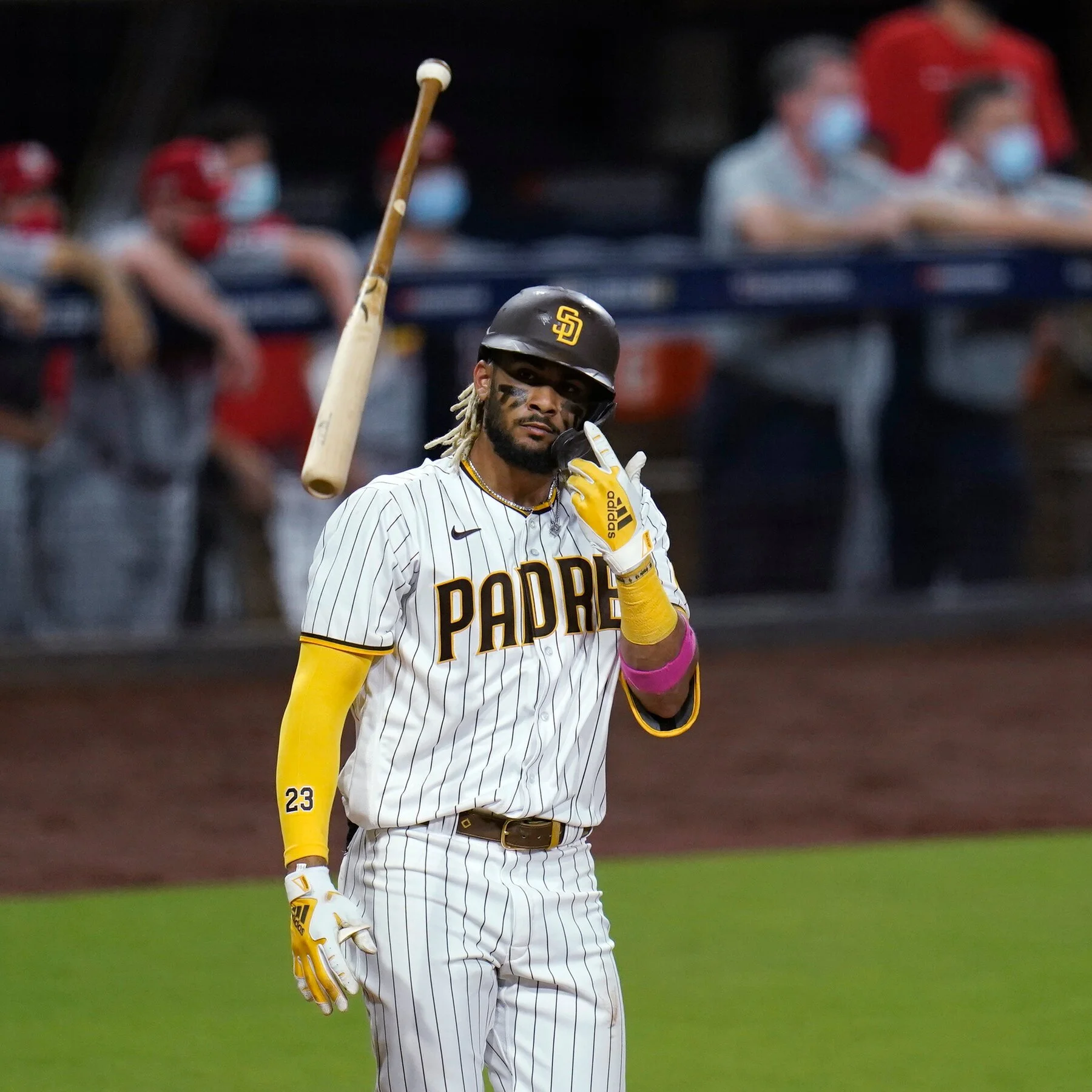 A baseball player in a San Diego Padres uniform with number 23, wearing batting gloves, a helmet, and with a bat resting on his shoulder, stands on the field near the dugout during a game.