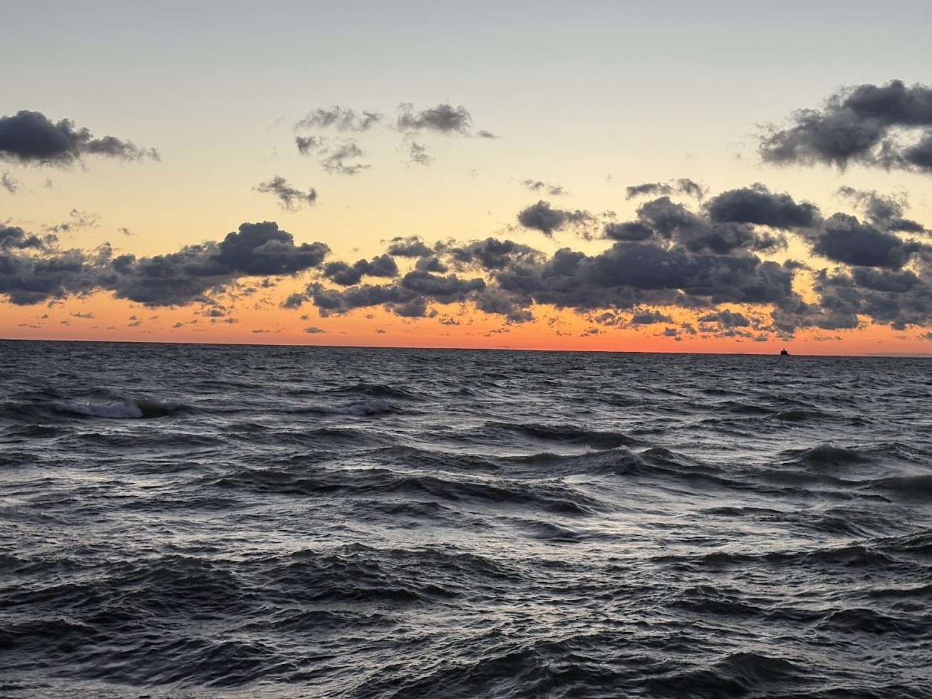 Ocean at sunset with dark clouds in the sky and a distant ship on the horizon.
