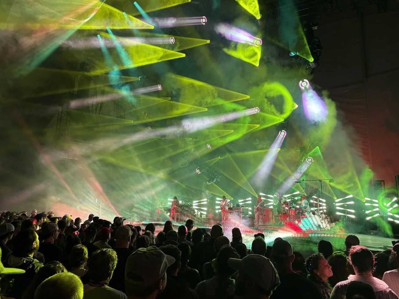 A live concert with a band performing on stage, illuminated by colorful green and yellow stage lights, with an audience watching.