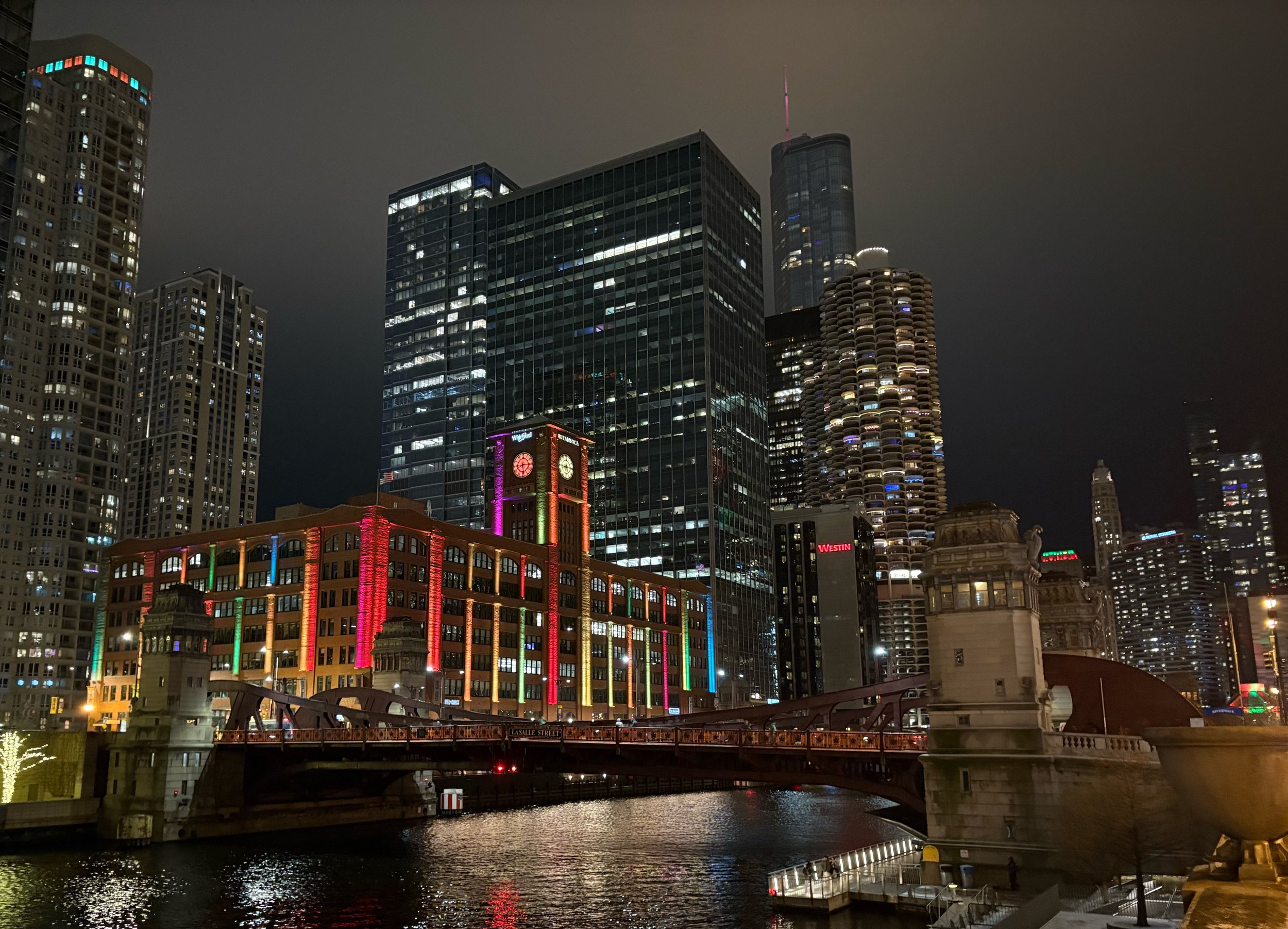 Nighttime cityscape of downtown Chicago featuring bright lights, tall skyscrapers, and a bridge over the water.
