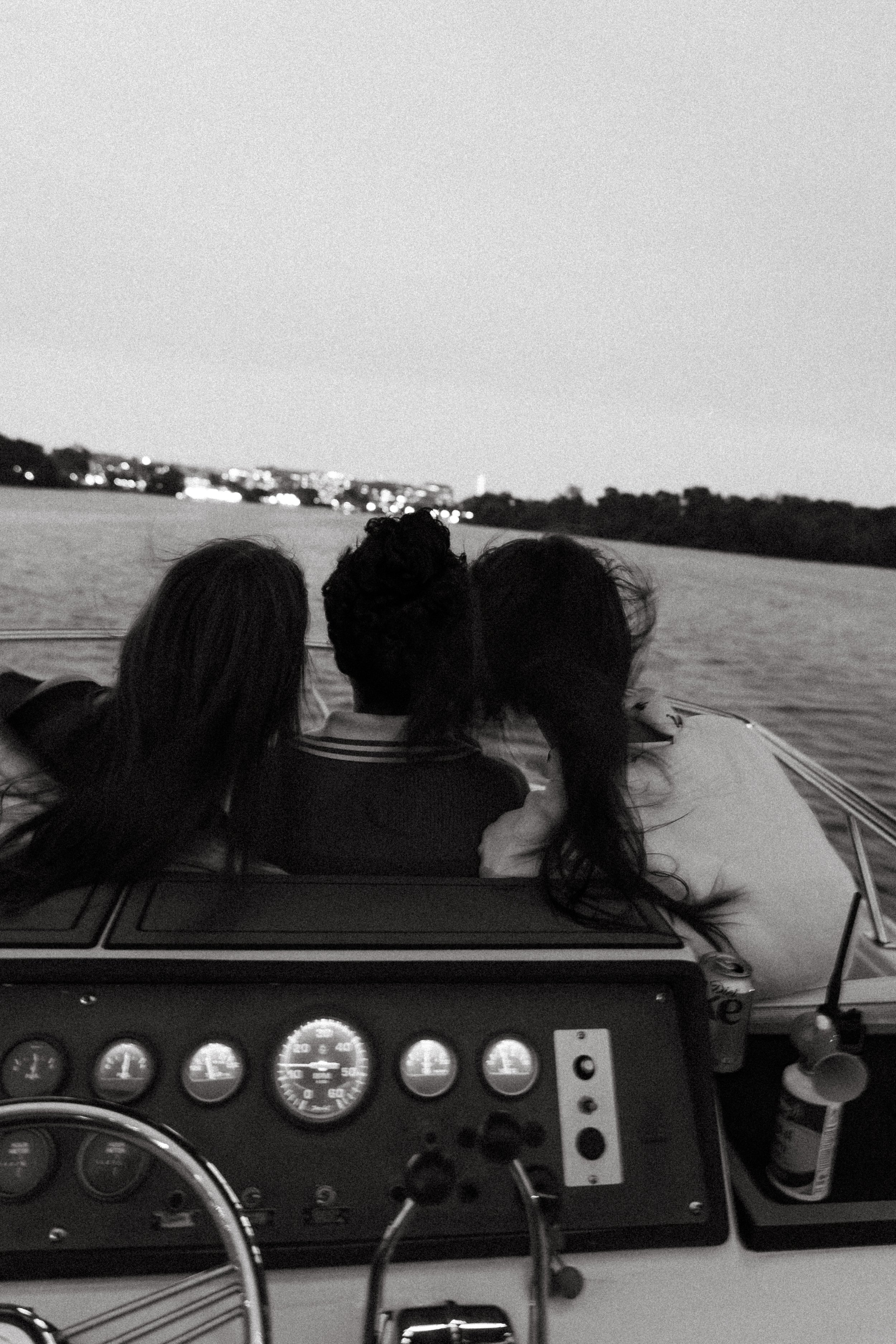 Three women sitting closely together at the front of a boat, looking out at the water and distant shoreline during dusk or night. Yacht cruise Washington D.C.
