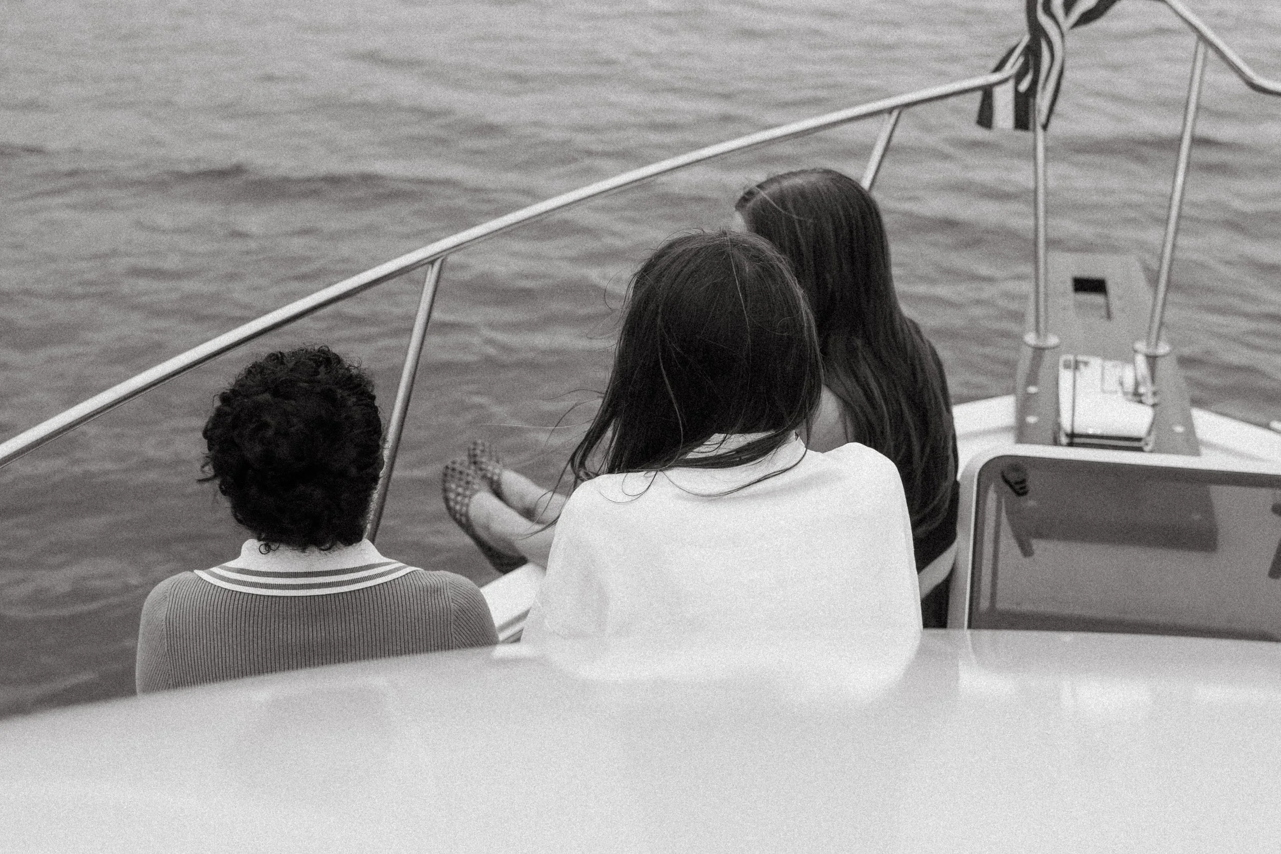 Three people sitting on a boat, looking out at the water, with their backs to the camera, black and white photo. Yacht cruise in D.C.