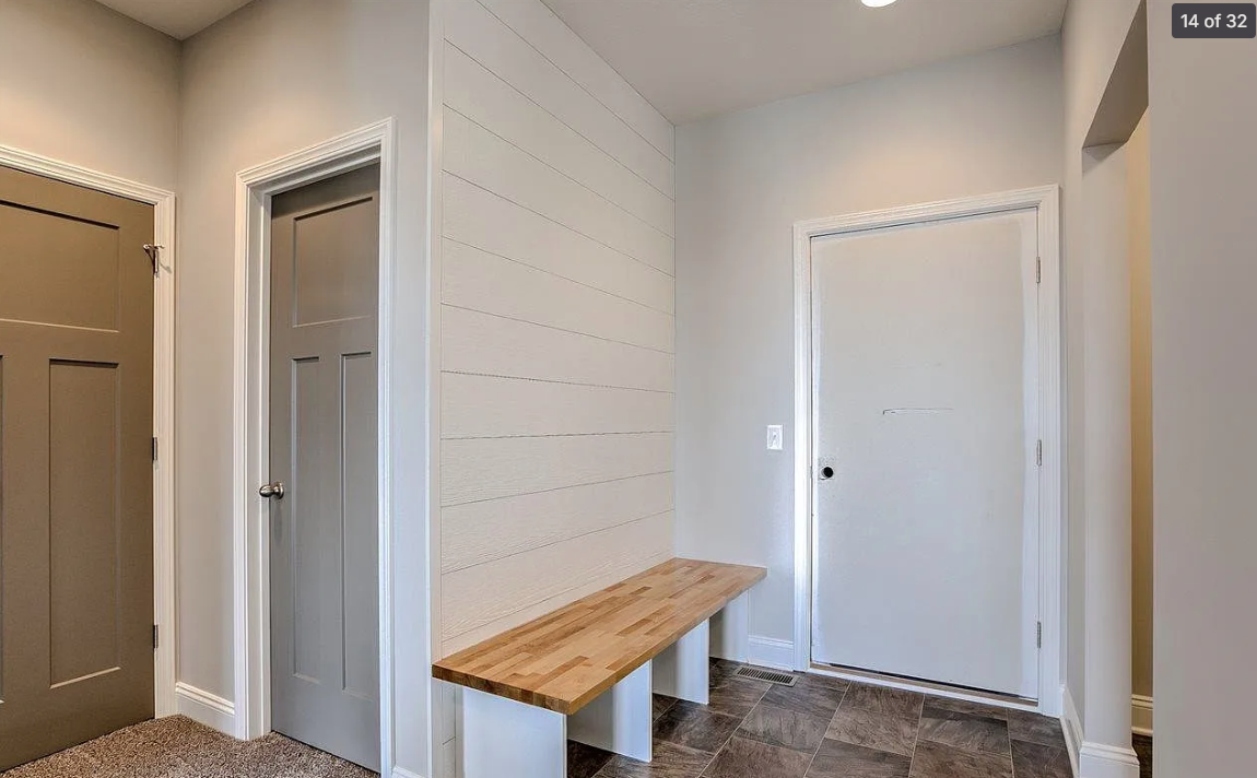 Entryway with white door, two gray interior doors, a wooden bench, and tile and carpet flooring.