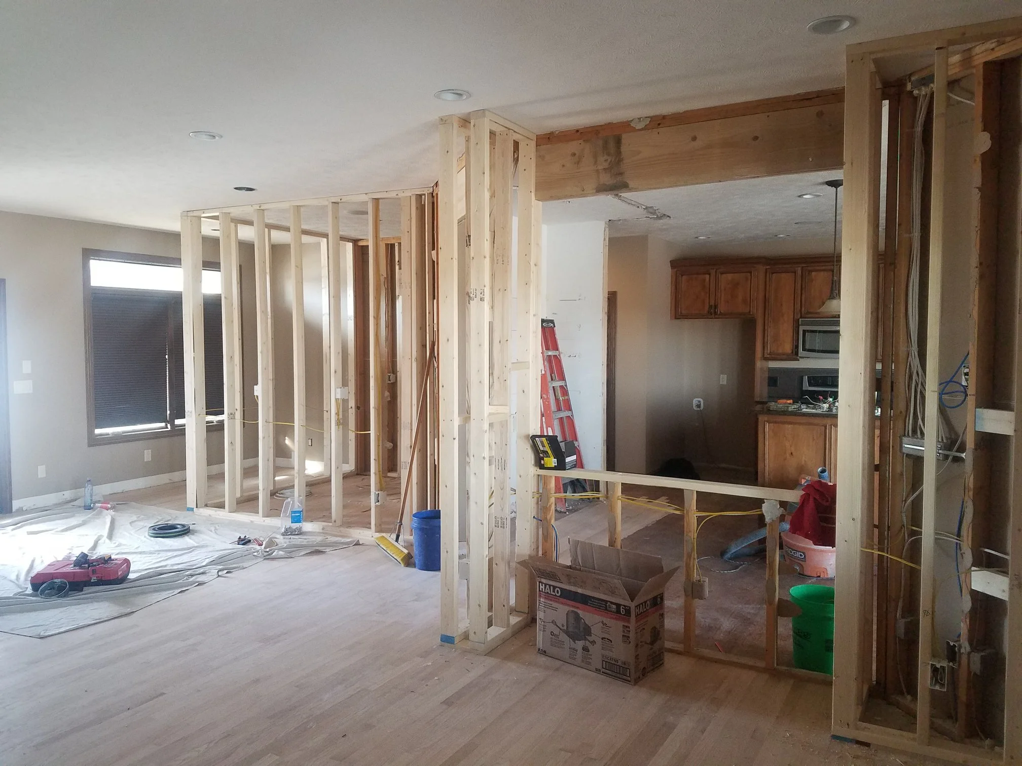 Interior view of a house under renovation with exposed wooden framing, construction tools, and materials on the floor.