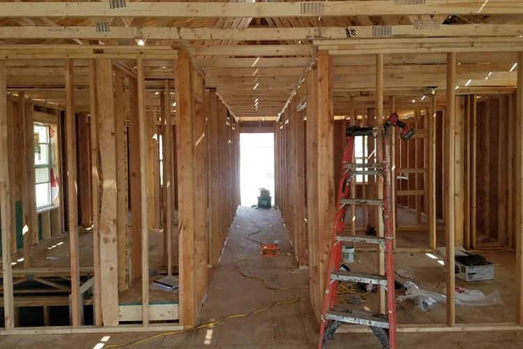 Interior view of a house under construction showing wooden framing, a ladder, and construction tools.