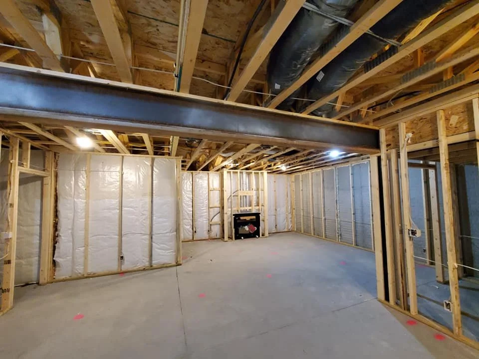 Undeveloped basement with exposed wooden framing, insulation, electrical wiring, and ductwork, ready for finishing.