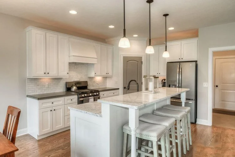 Modern kitchen with white cabinets, marble island, stainless steel appliances, and hanging pendant lights.