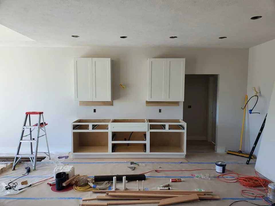 Kitchen under construction with white cabinets, construction tools, and materials on the floor.