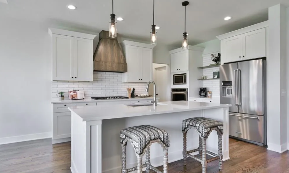 Modern kitchen with white cabinets, a large island with seating, stainless steel refrigerator, and pendant lighting.