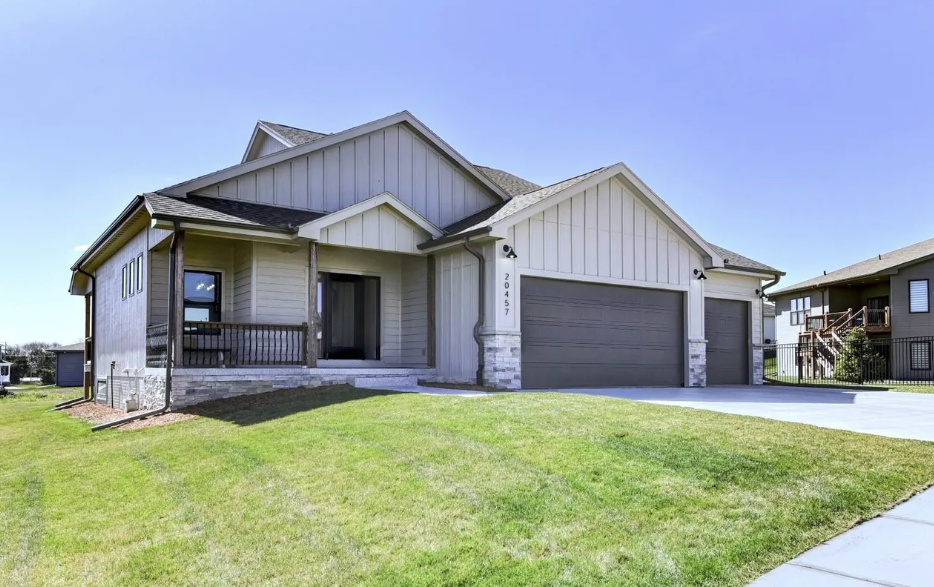 A modern two-story house with a gray garage door, white siding, a front porch, and a well-maintained lawn under a clear blue sky.