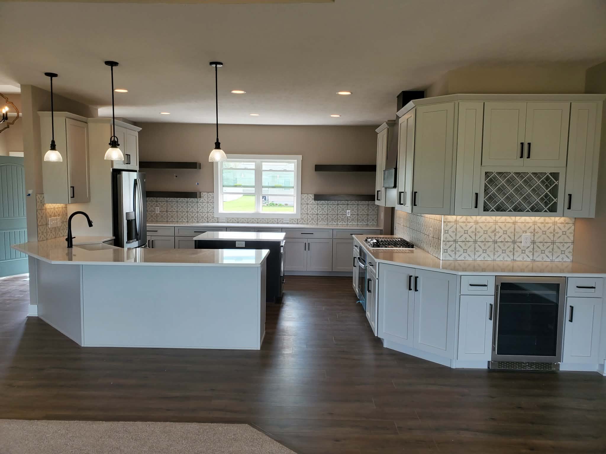 Modern kitchen with white cabinets, black appliances, a kitchen island, pendant lighting, tiled backsplash, and wood flooring.