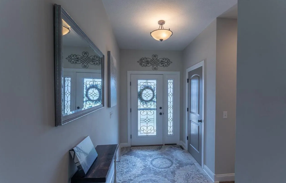 Foyer with a white door decorated with a holiday wreath, a mirror on the left wall, a small wooden table with a picture frame, a ceiling light fixture, and decorative wall art.
